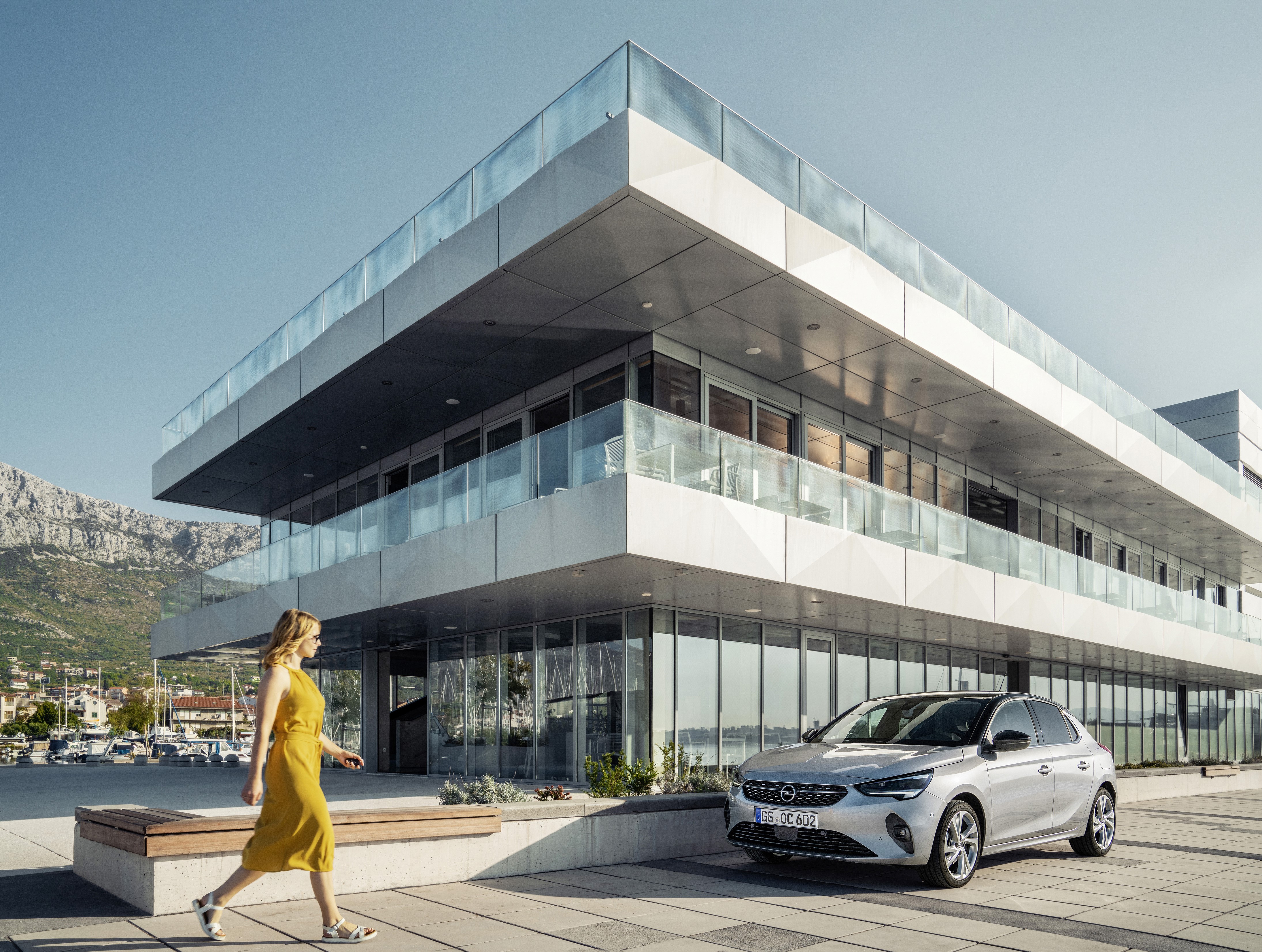 Woman walking by Opel Corsa in front of modern building HD Wallpaper