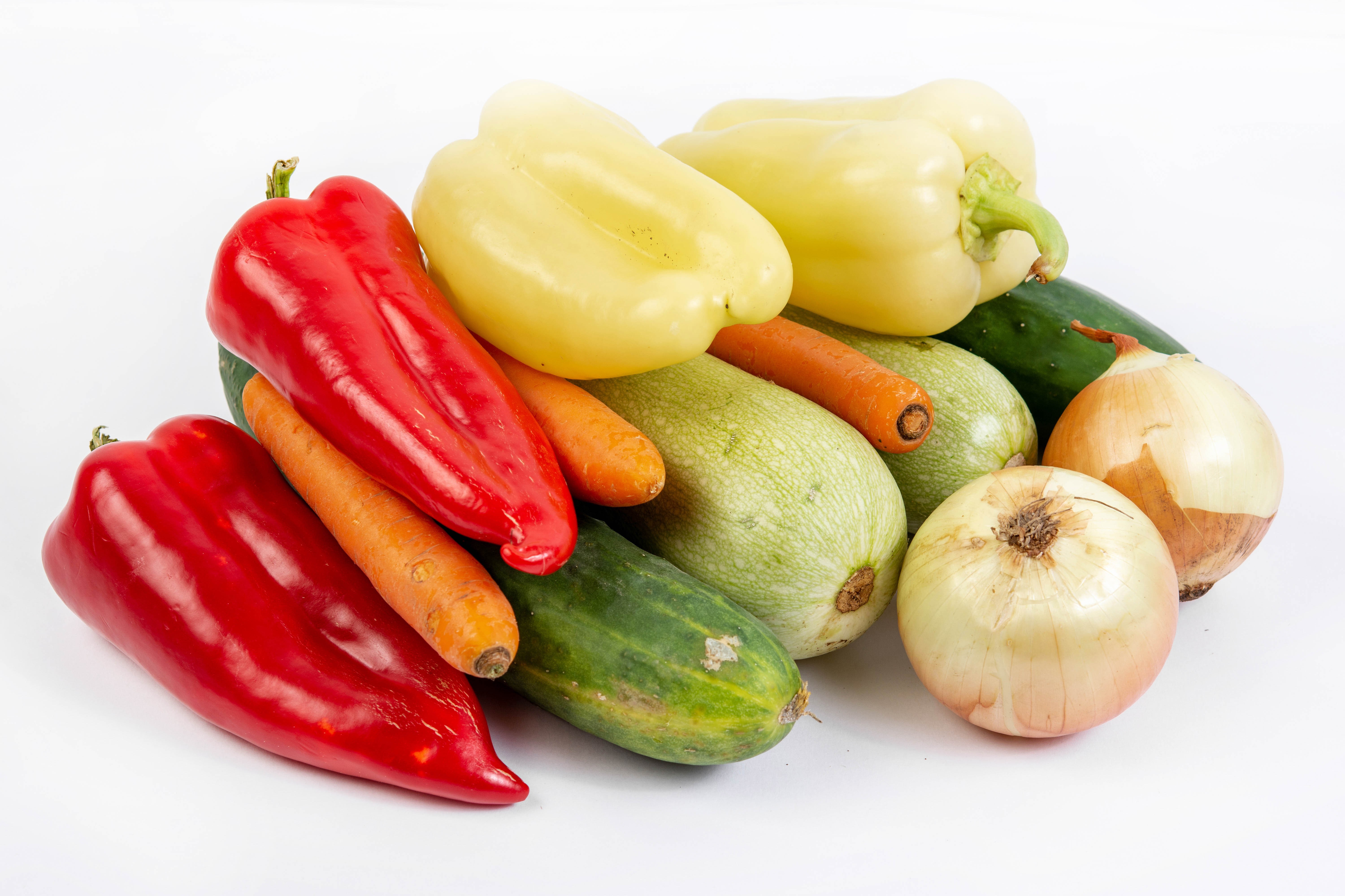 Assortment of fresh vegetables including peppers, carrots, cucumbers, zucchini, and onions on a white background HD Wallpaper