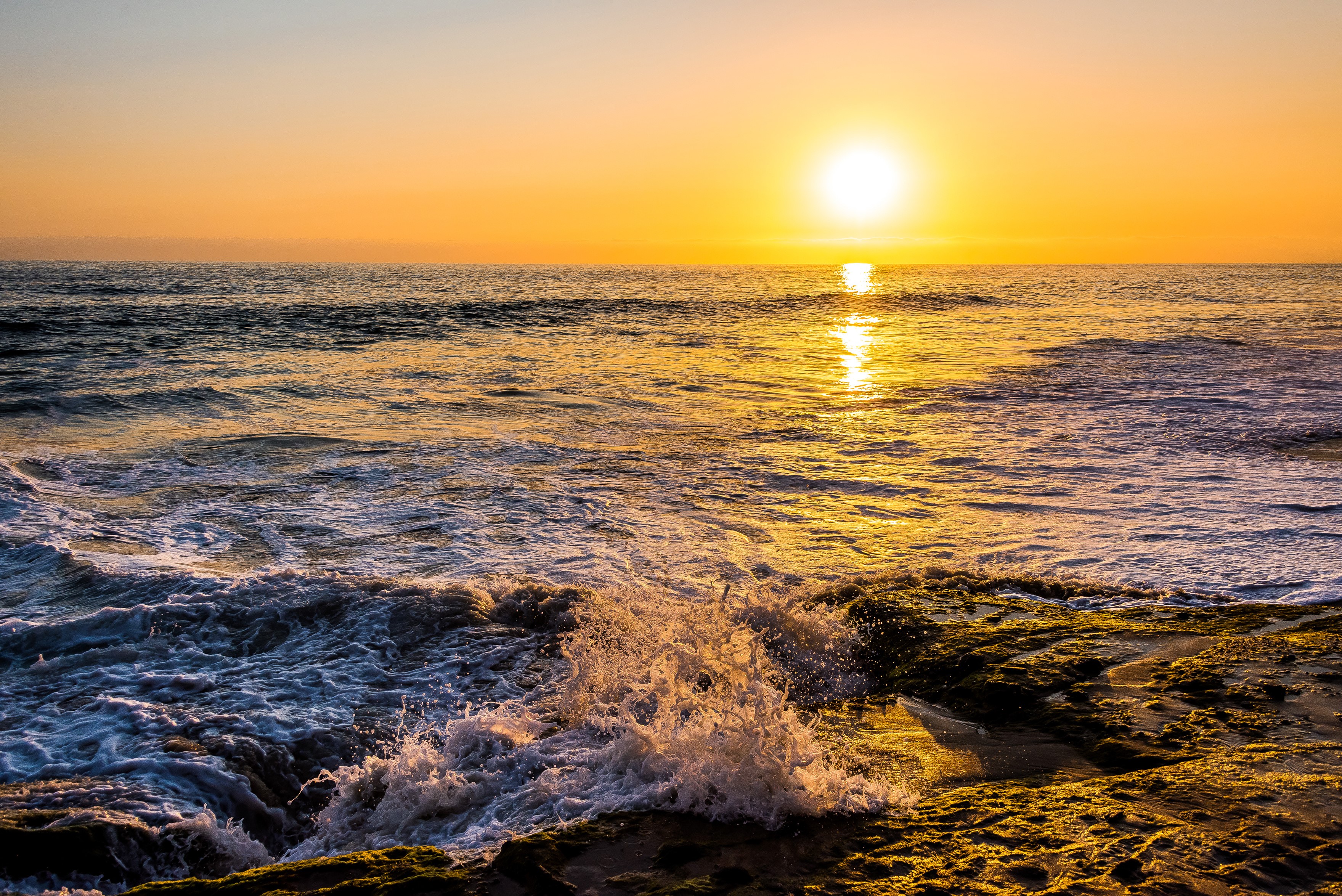Sunset over the ocean with waves crashing on rocks HD Wallpaper
