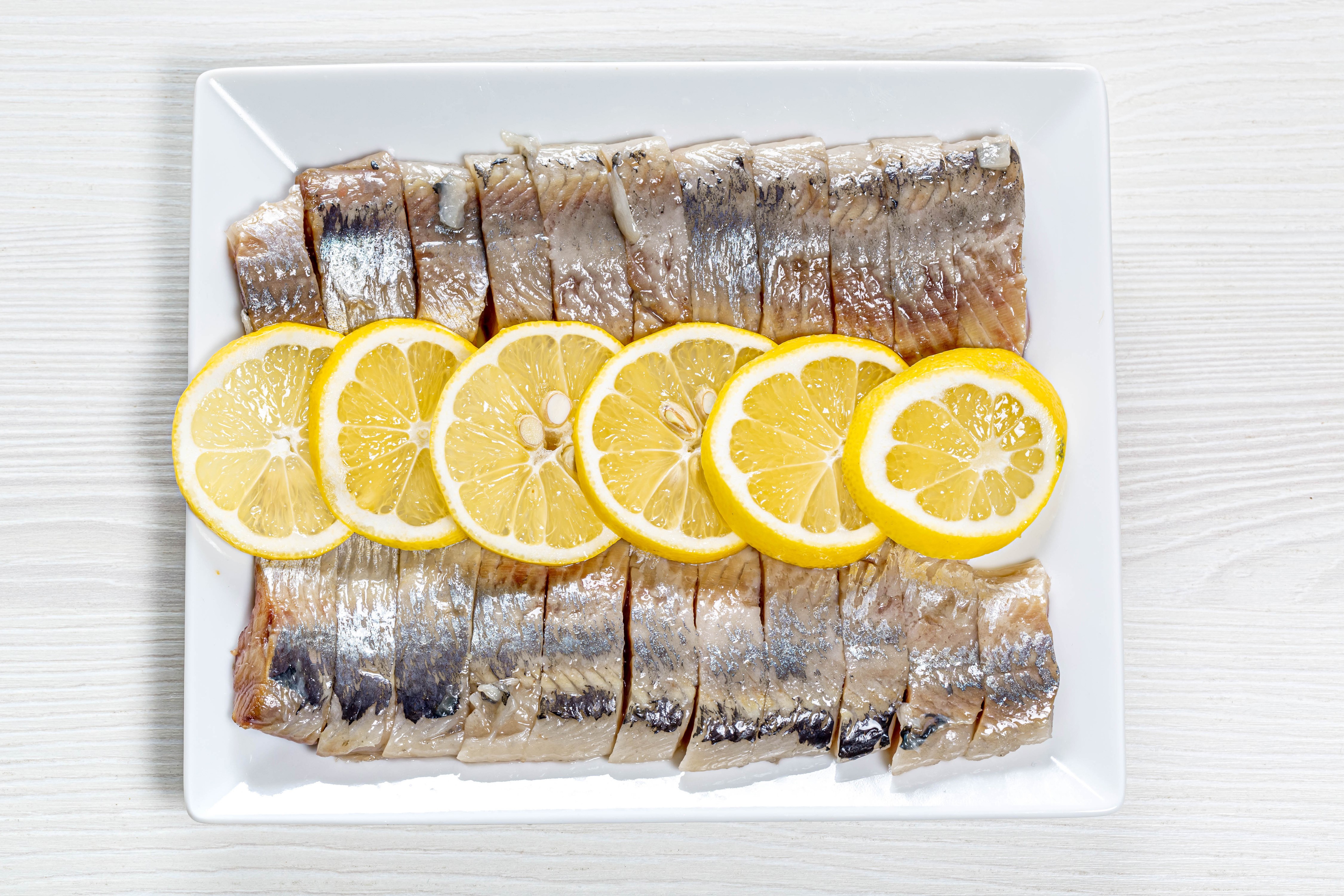 Sliced herring with lemon slices on a white plate HD Wallpaper
