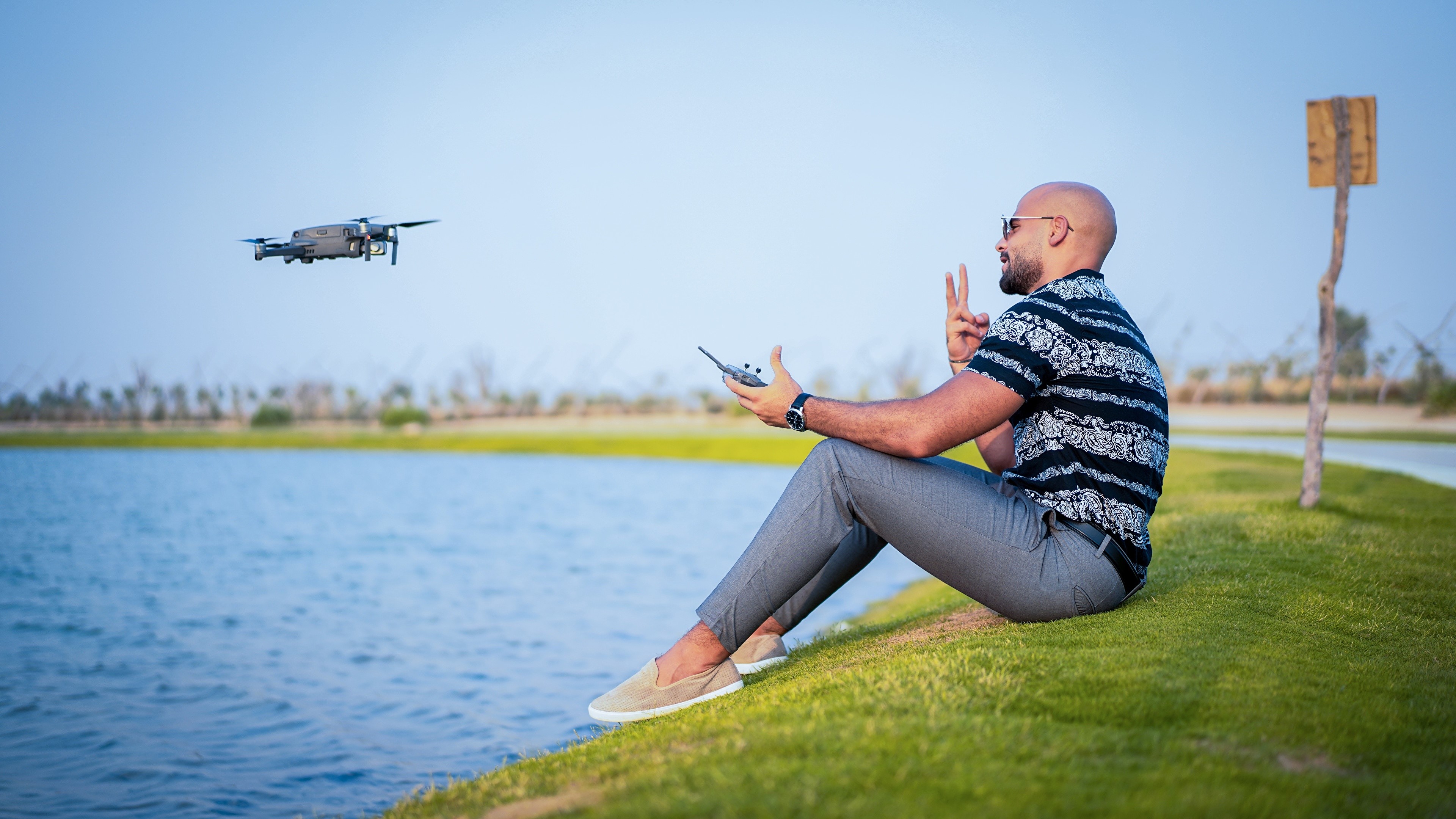 Man controlling a drone by a lake HD Wallpaper