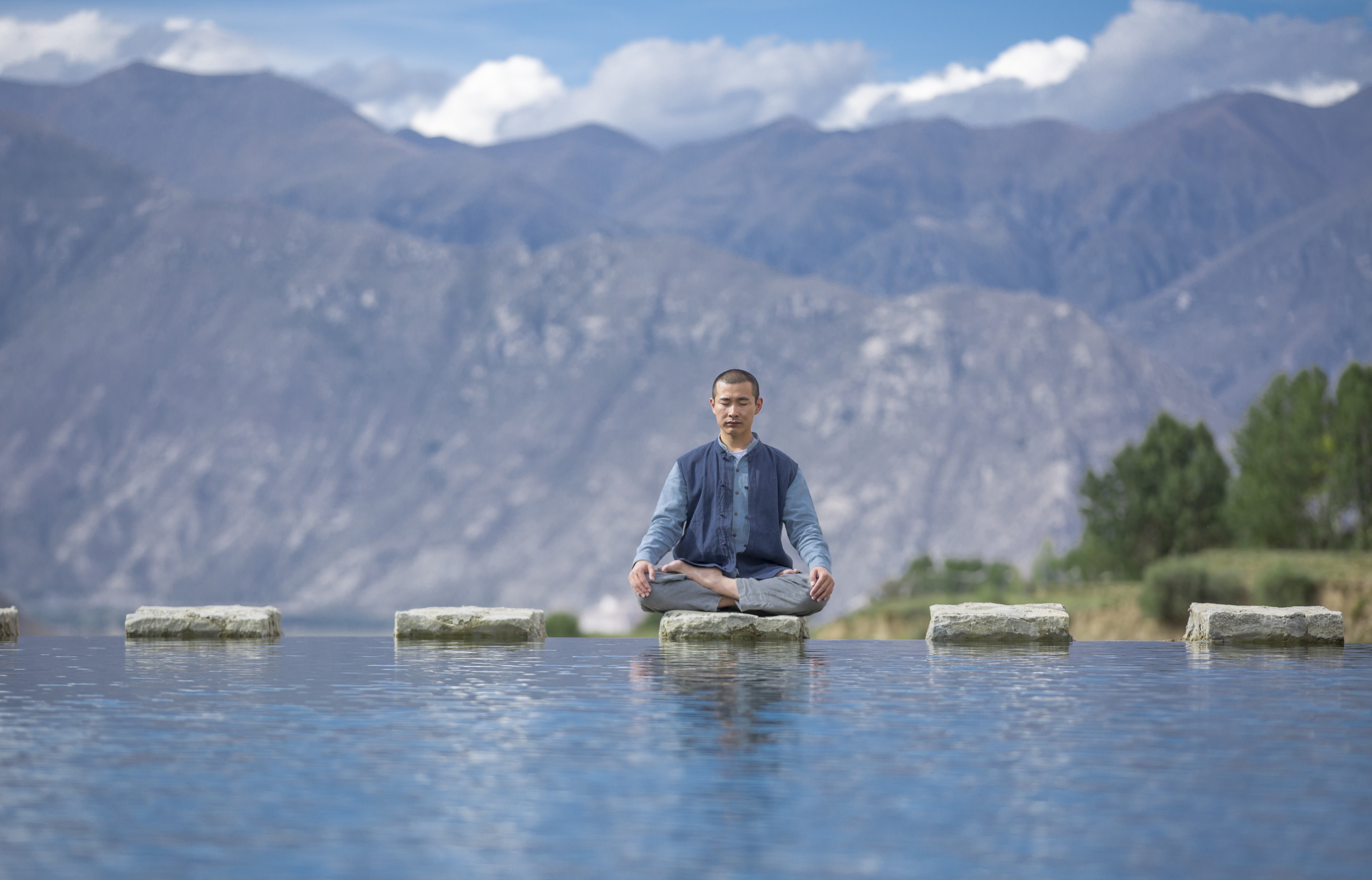 Man meditating in lotus position on stones in water HD Wallpaper