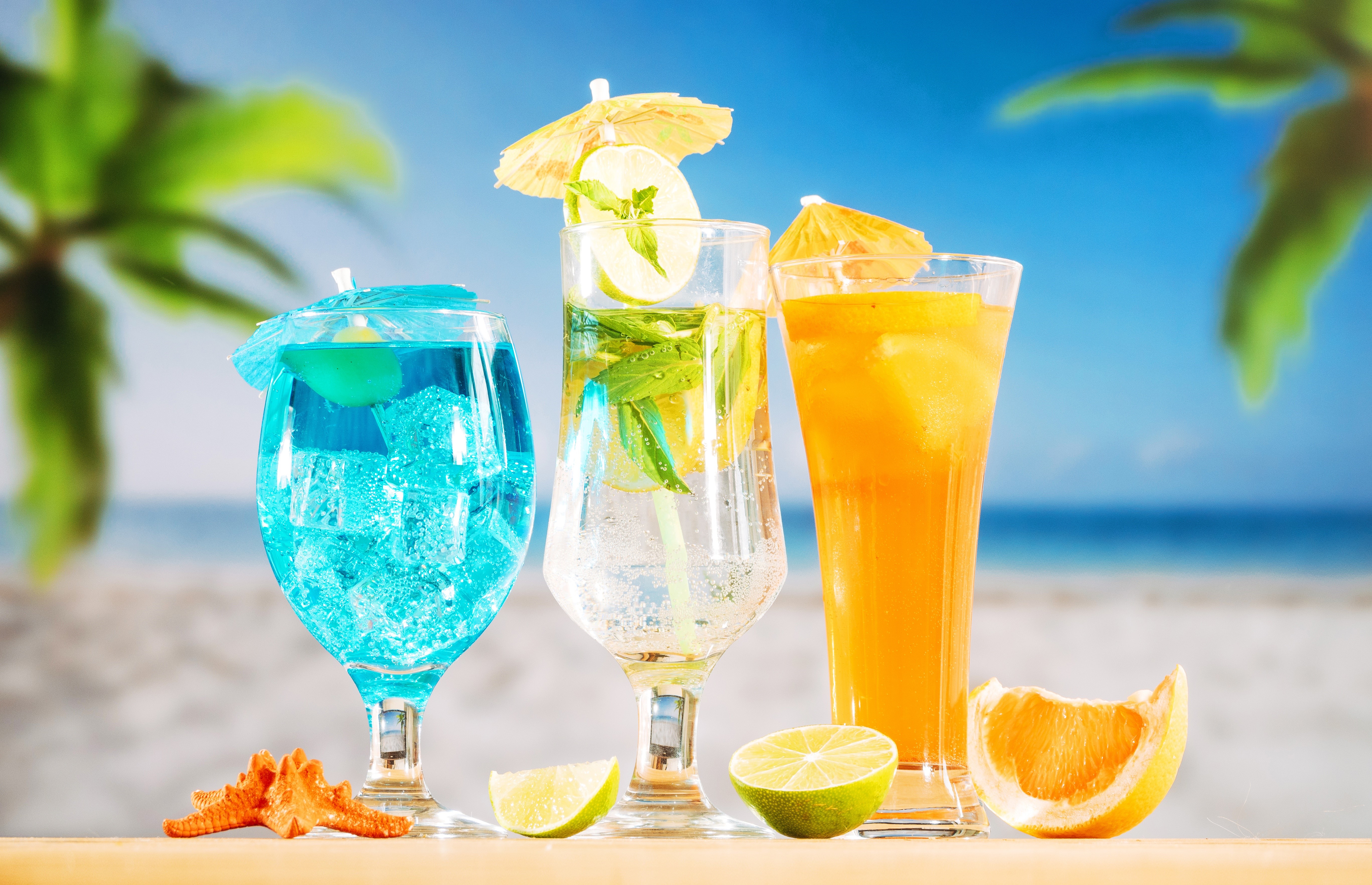 Three cocktails on a beach with palm trees HD Wallpaper