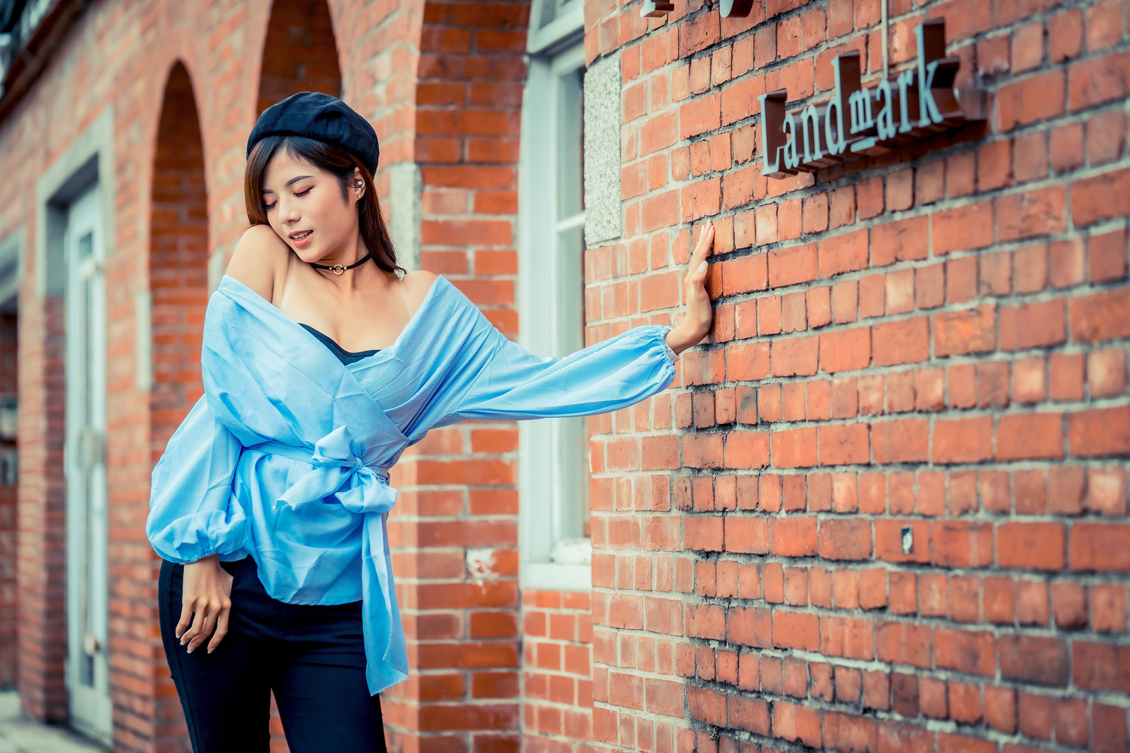Asian woman in blue blouse and beret leaning on brick wall HD Wallpaper