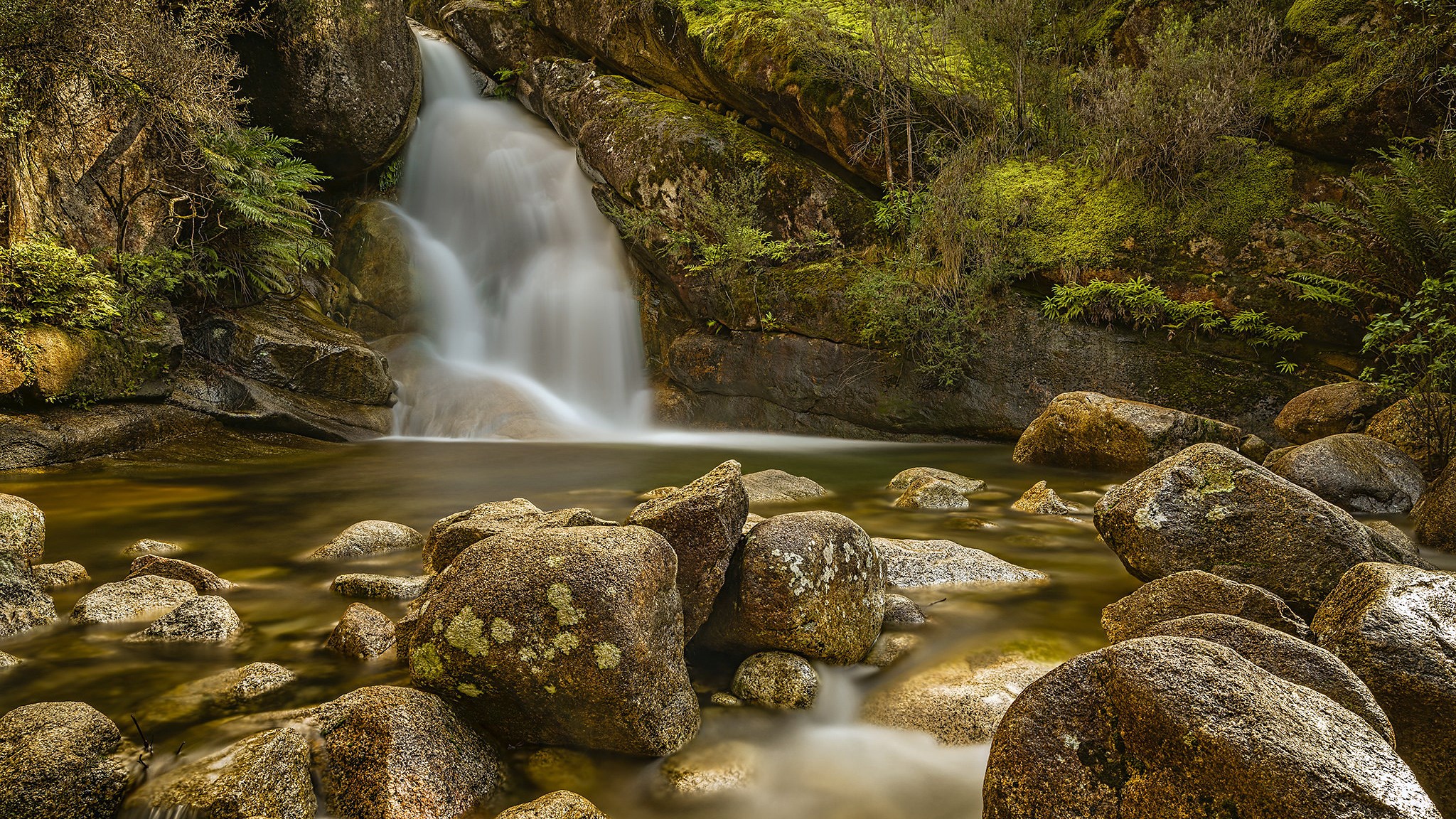 Waterfall cascading over rocks into a stream HD Wallpaper