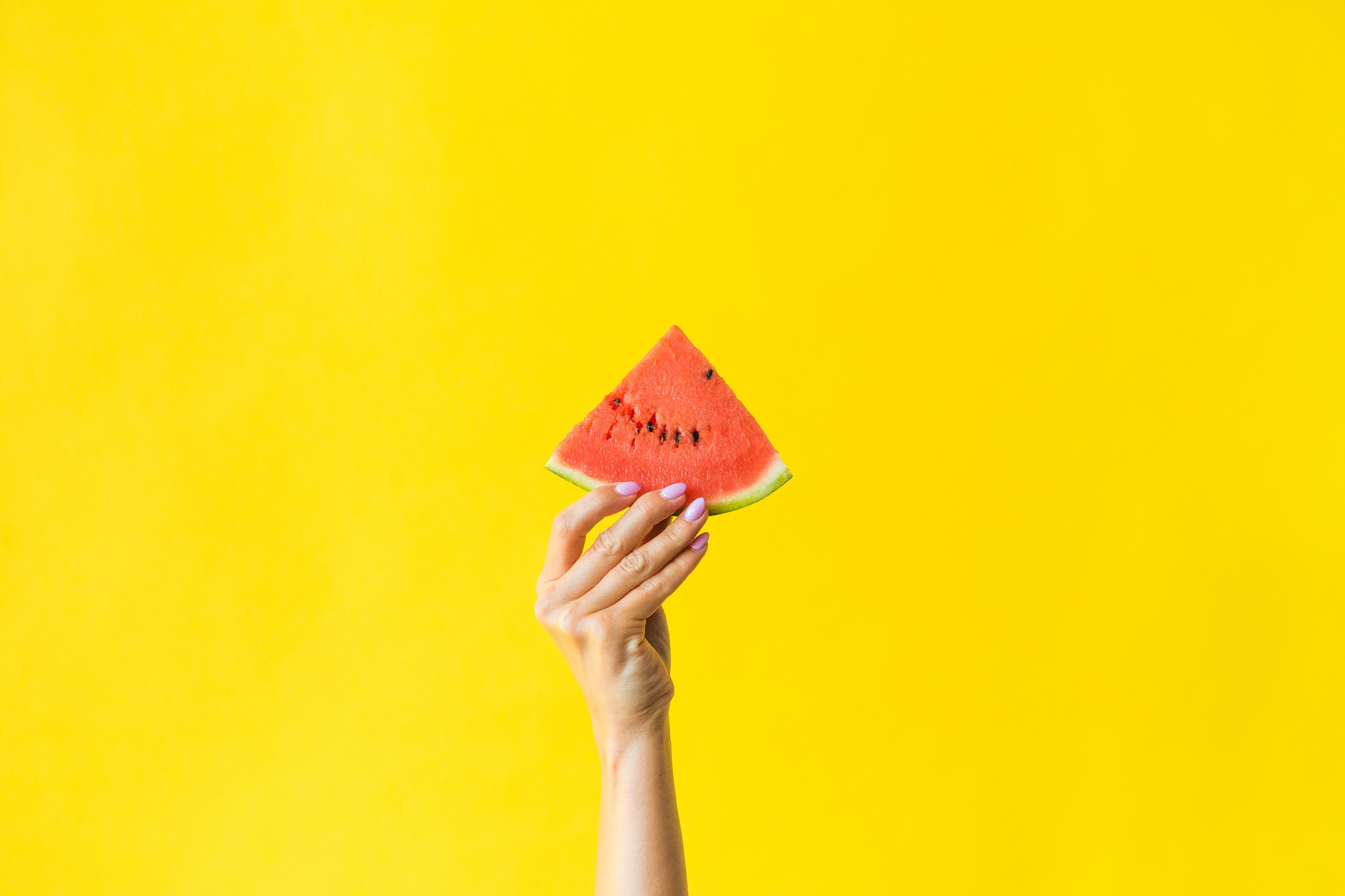 Hand holding a slice of watermelon on a yellow background HD Wallpaper