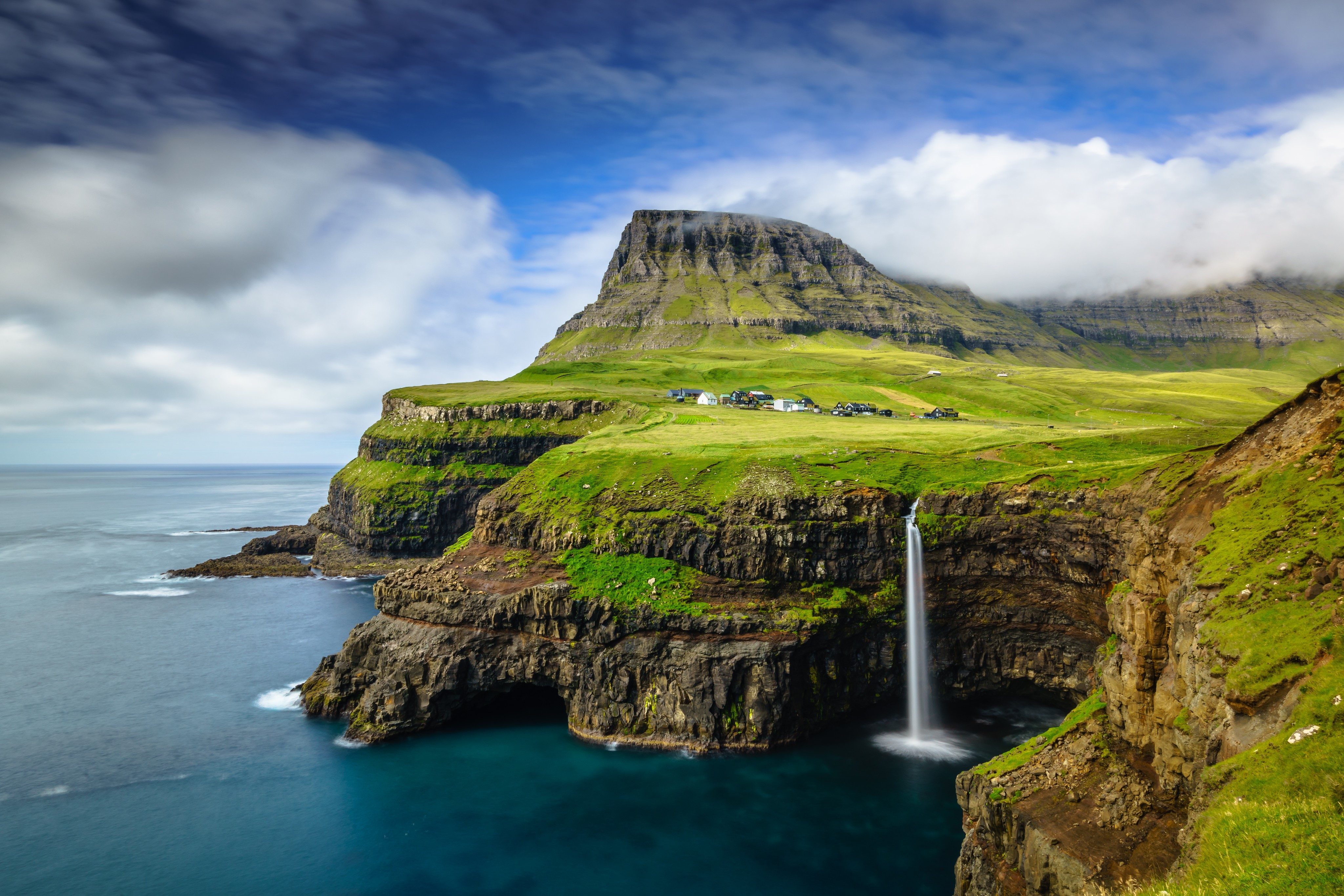 Waterfall cascading from green cliffs into the ocean HD Wallpaper
