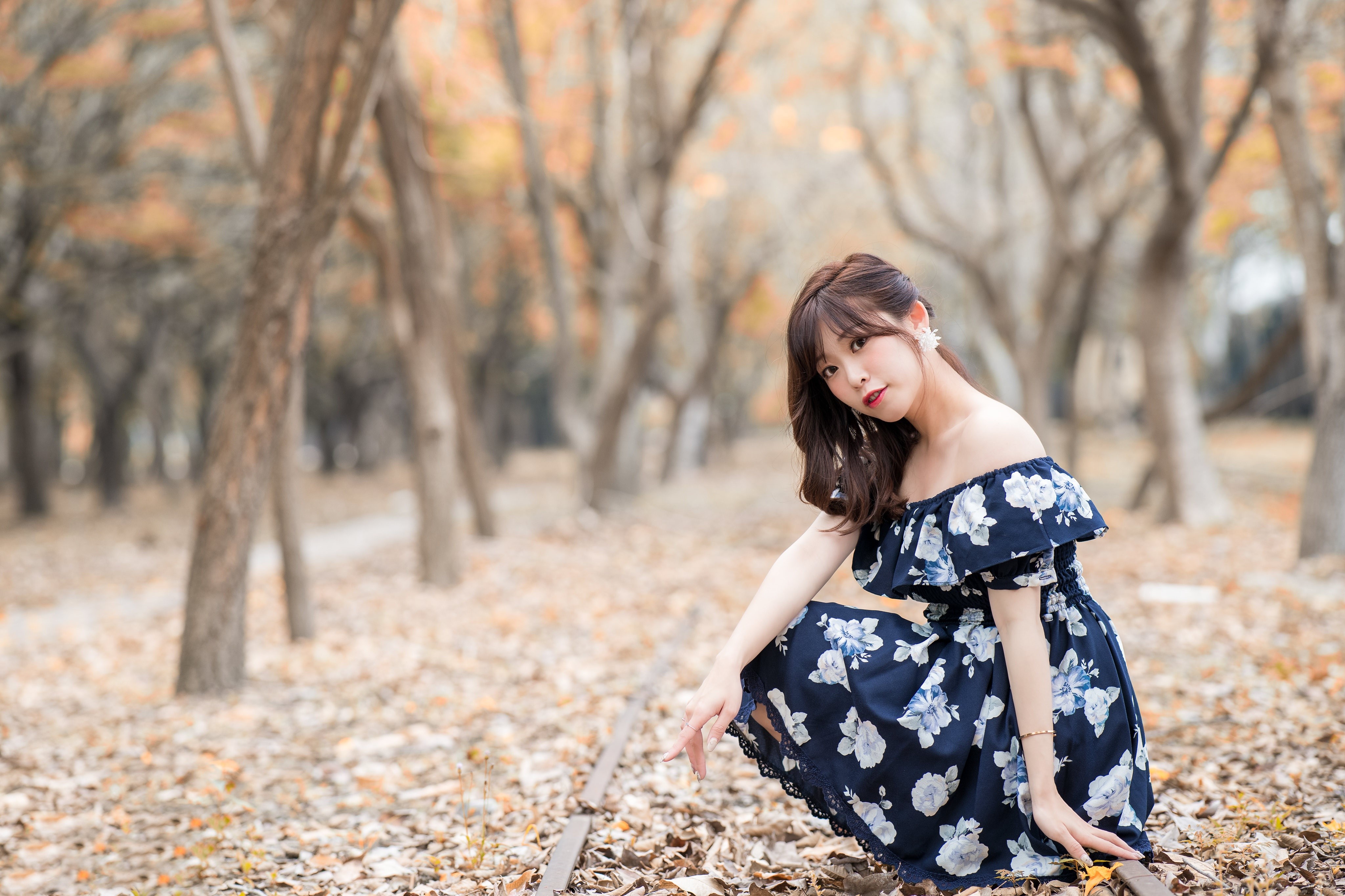Asian woman in floral dress crouching near train tracks HD Wallpaper