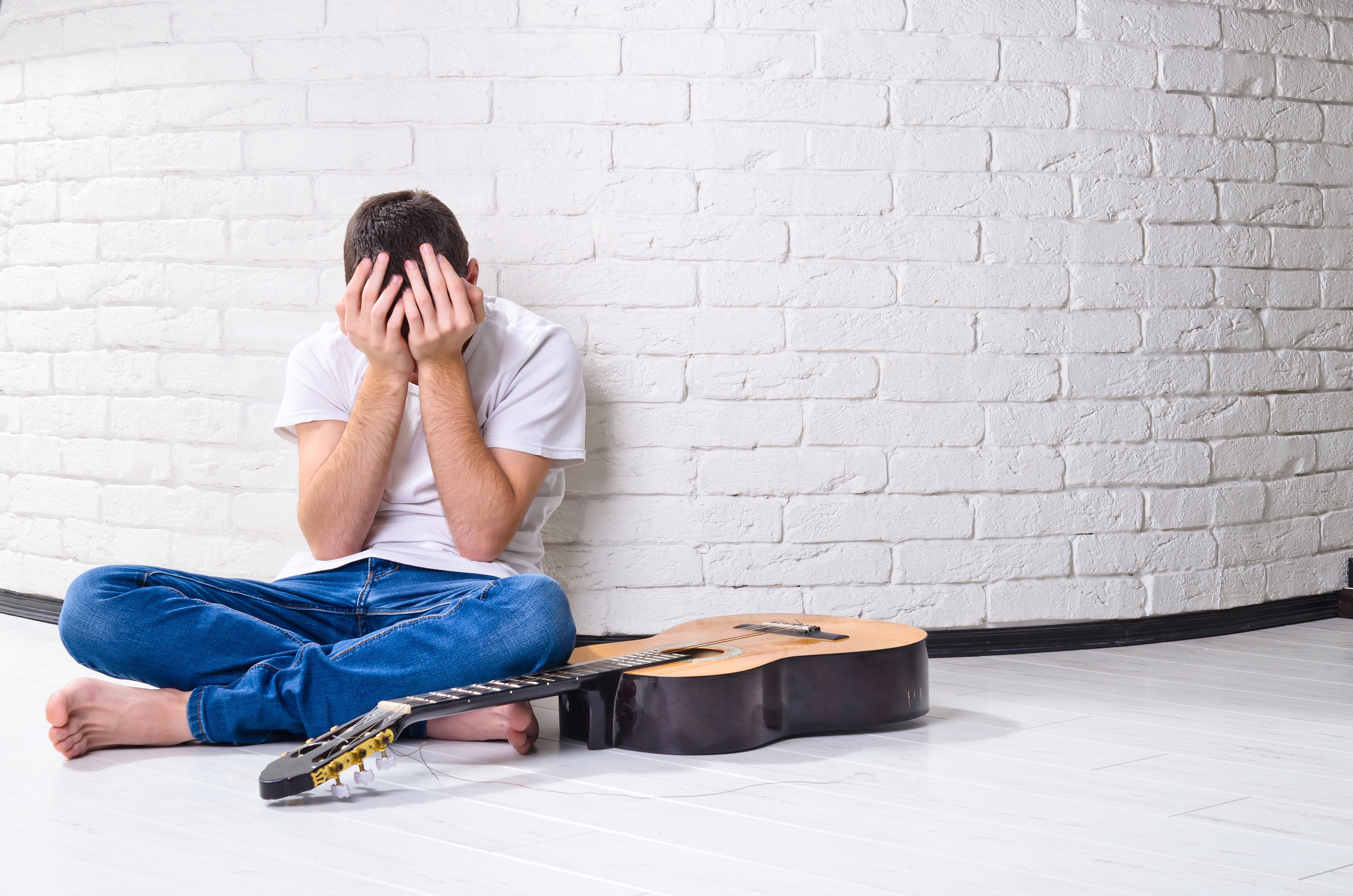 Man sitting with guitar, covering face HD Wallpaper