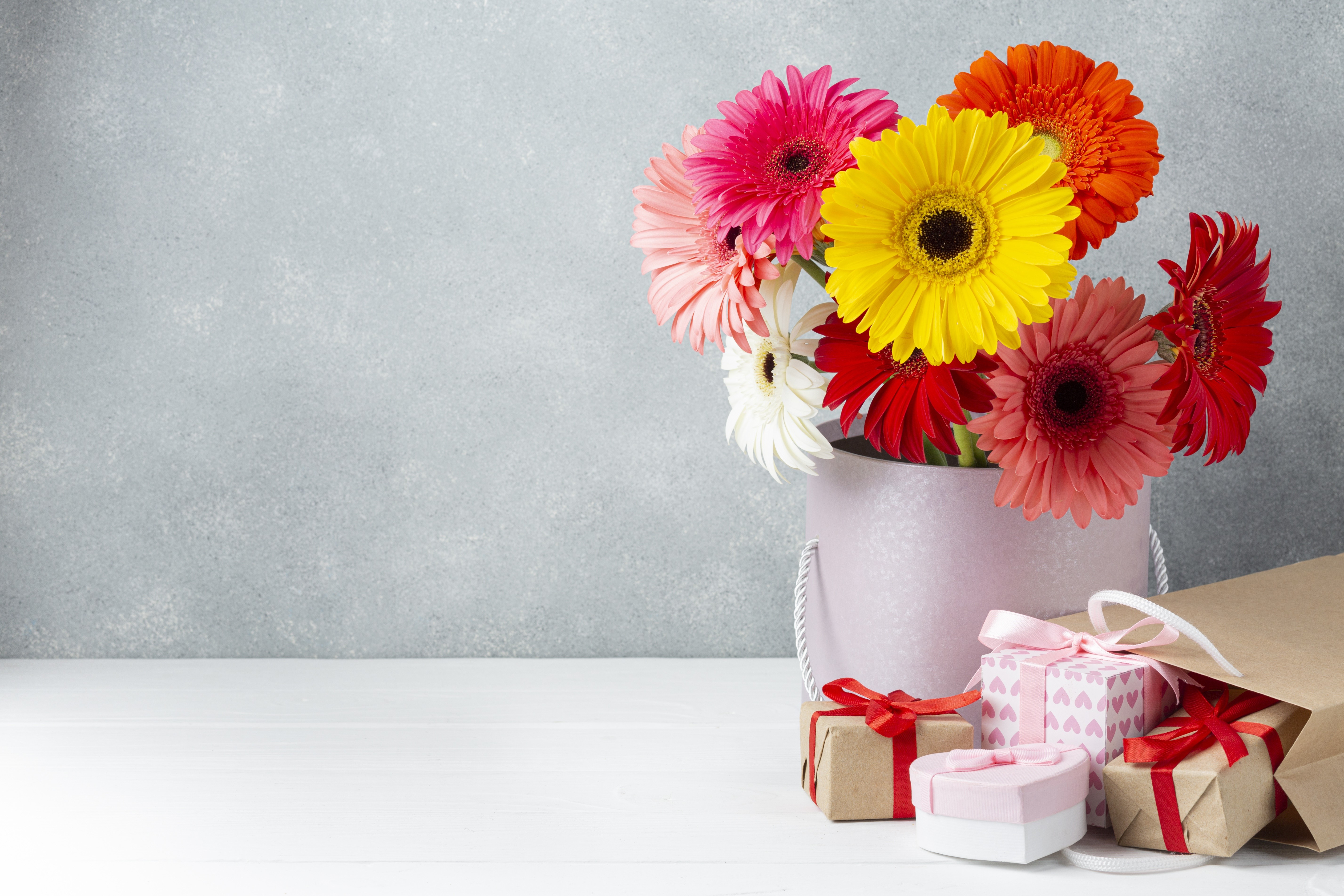 Gerbera bouquet in a vase with gifts and paper bag HD Wallpaper
