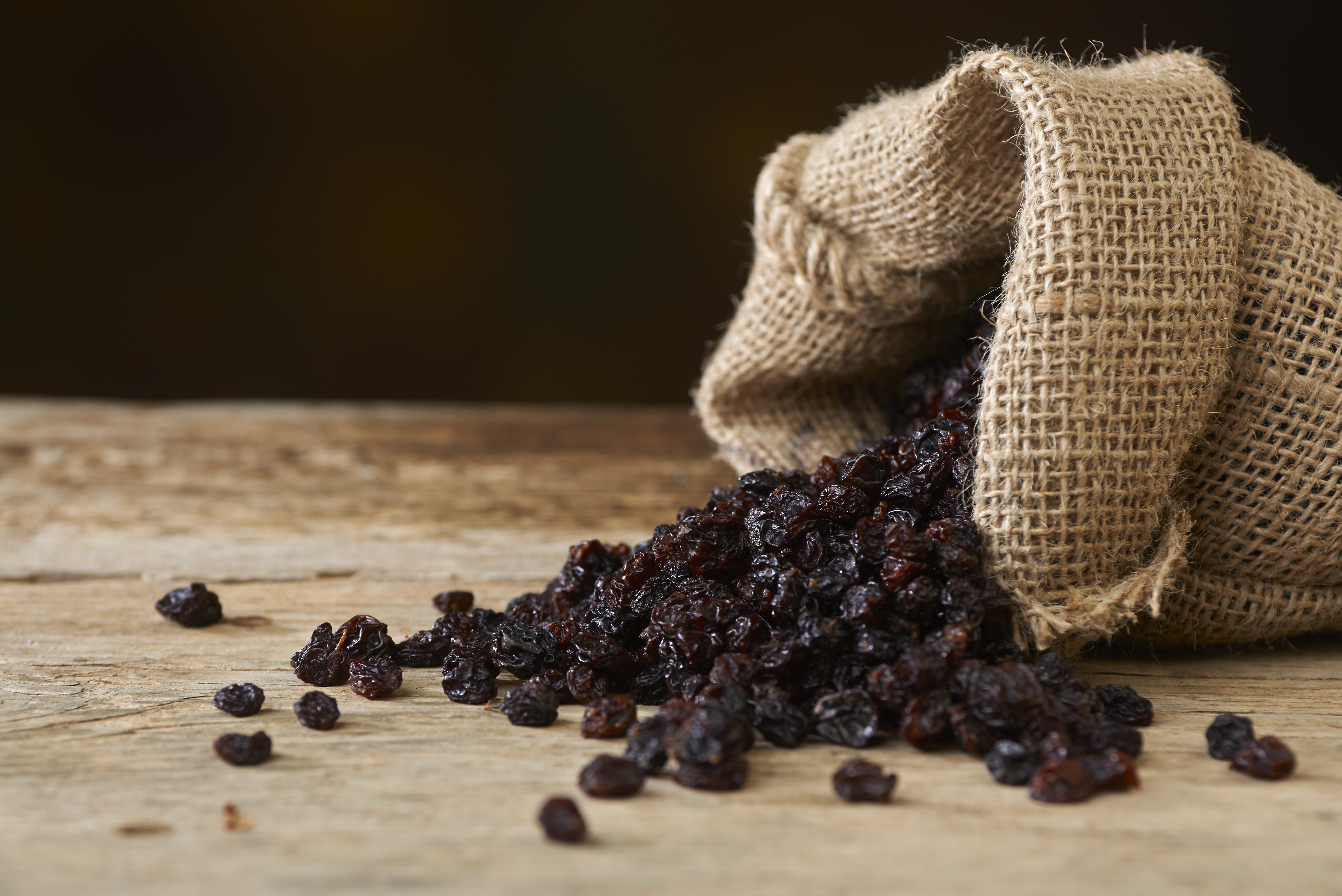 Raisins spilling from a burlap sack onto a wooden table HD Wallpaper