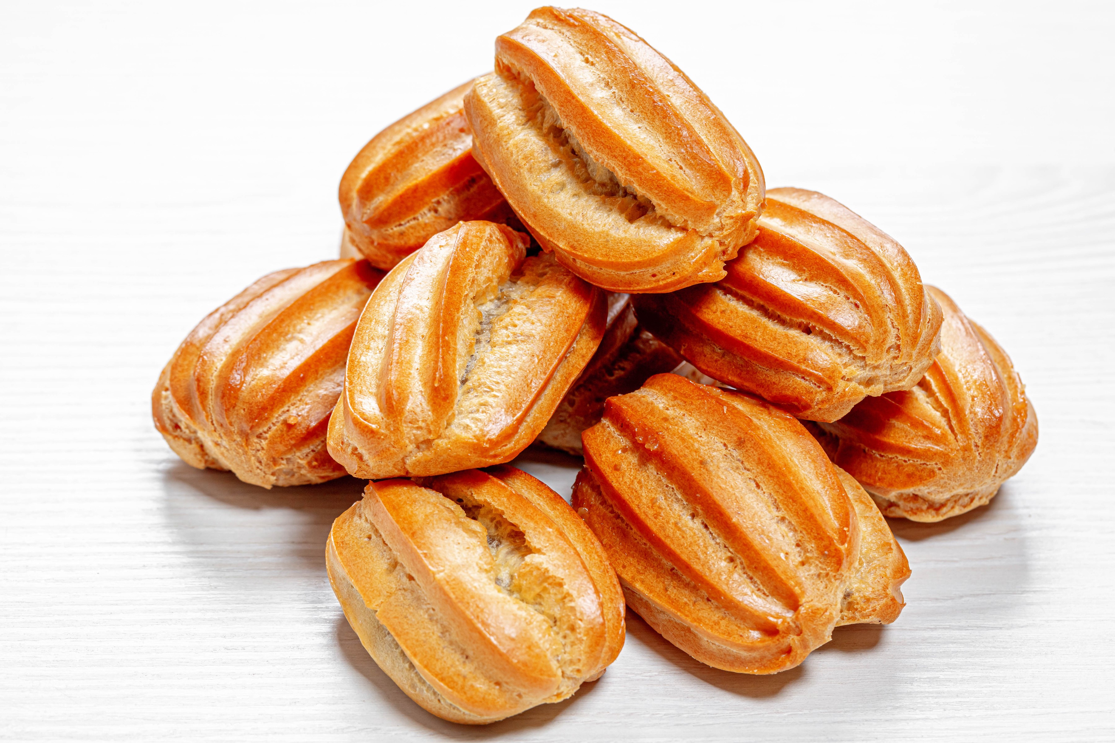 Pile of golden brown eclairs on a white surface HD Wallpaper