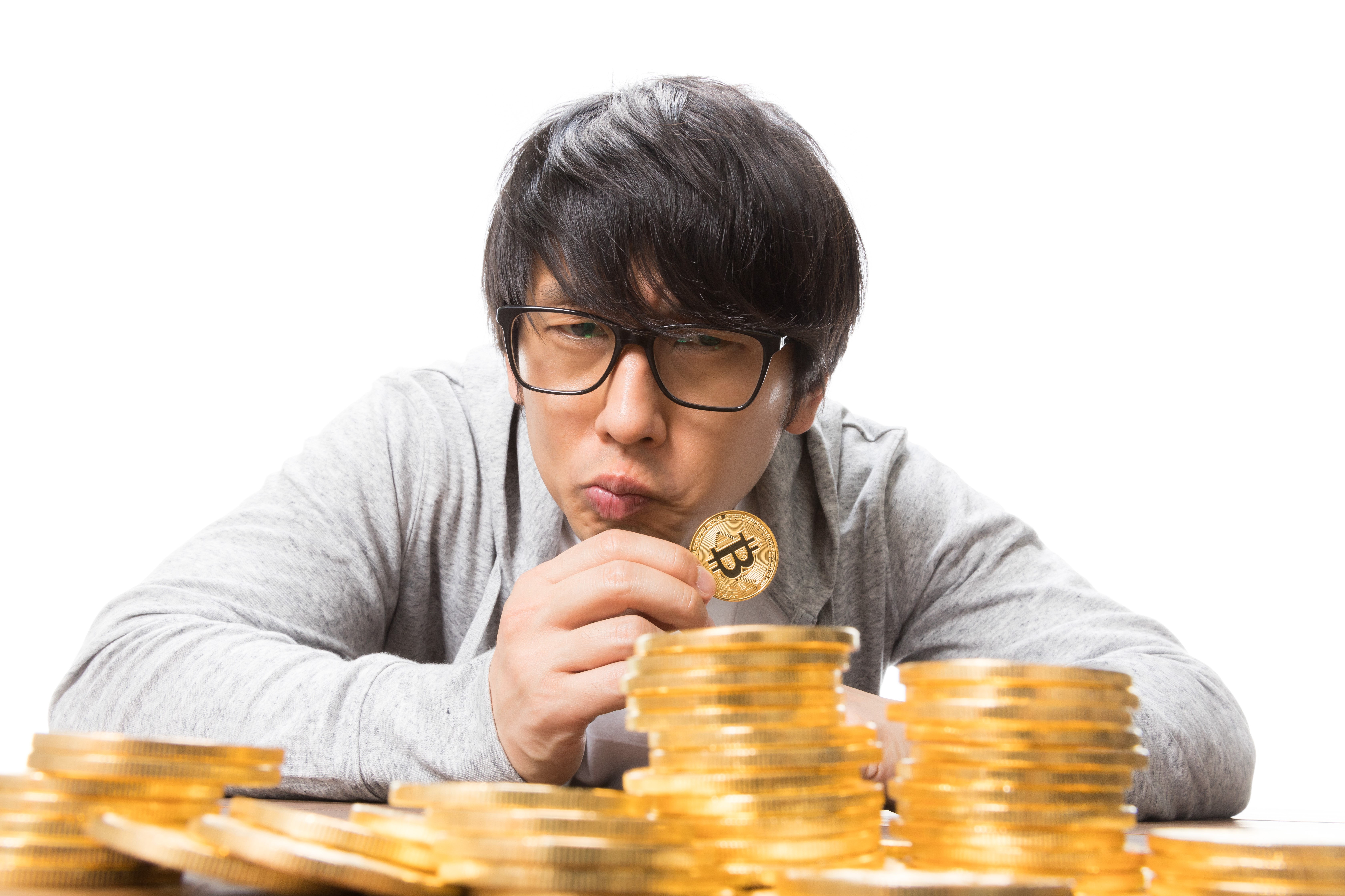 Asian man in glasses holding Bitcoin coin with stacks of coins HD Wallpaper