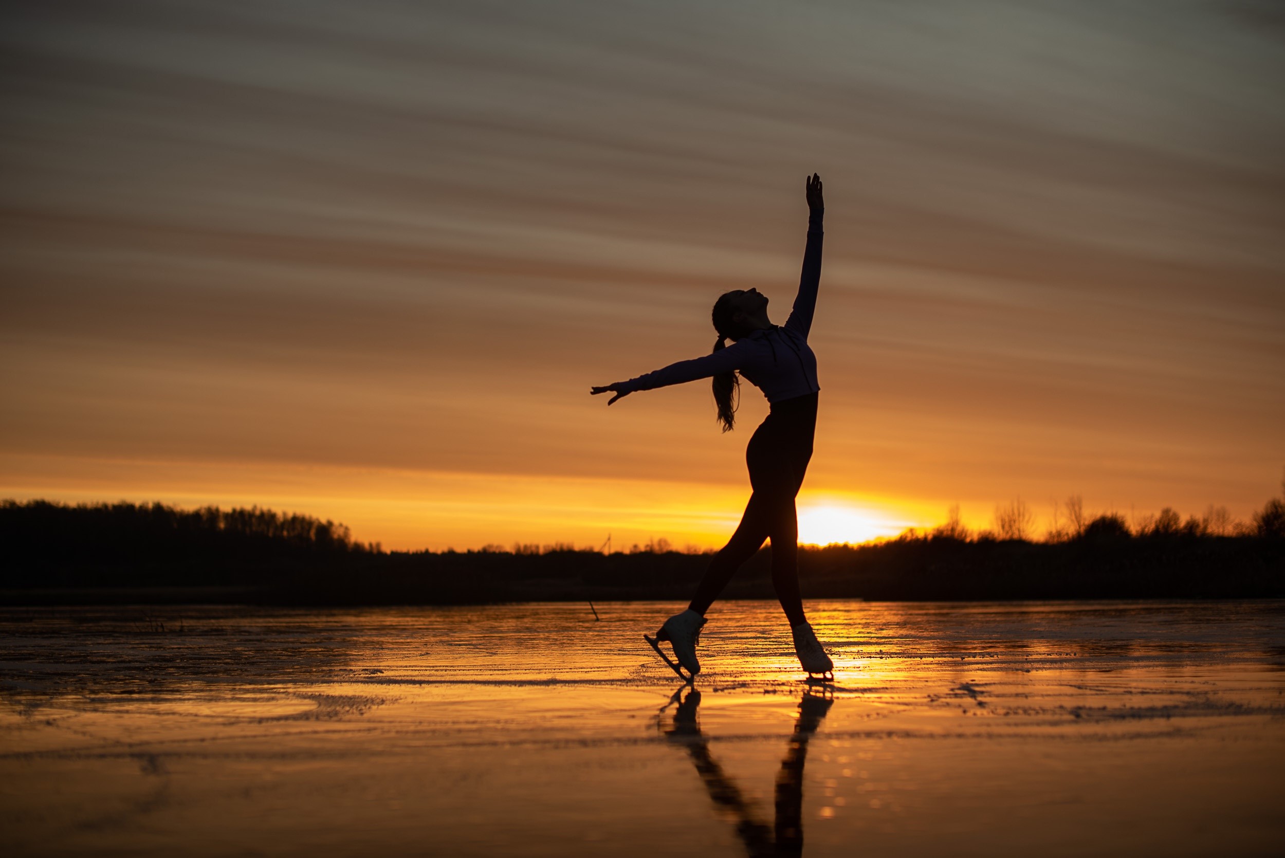 Figure skater silhouetted against a sunset over a frozen lake HD Wallpaper