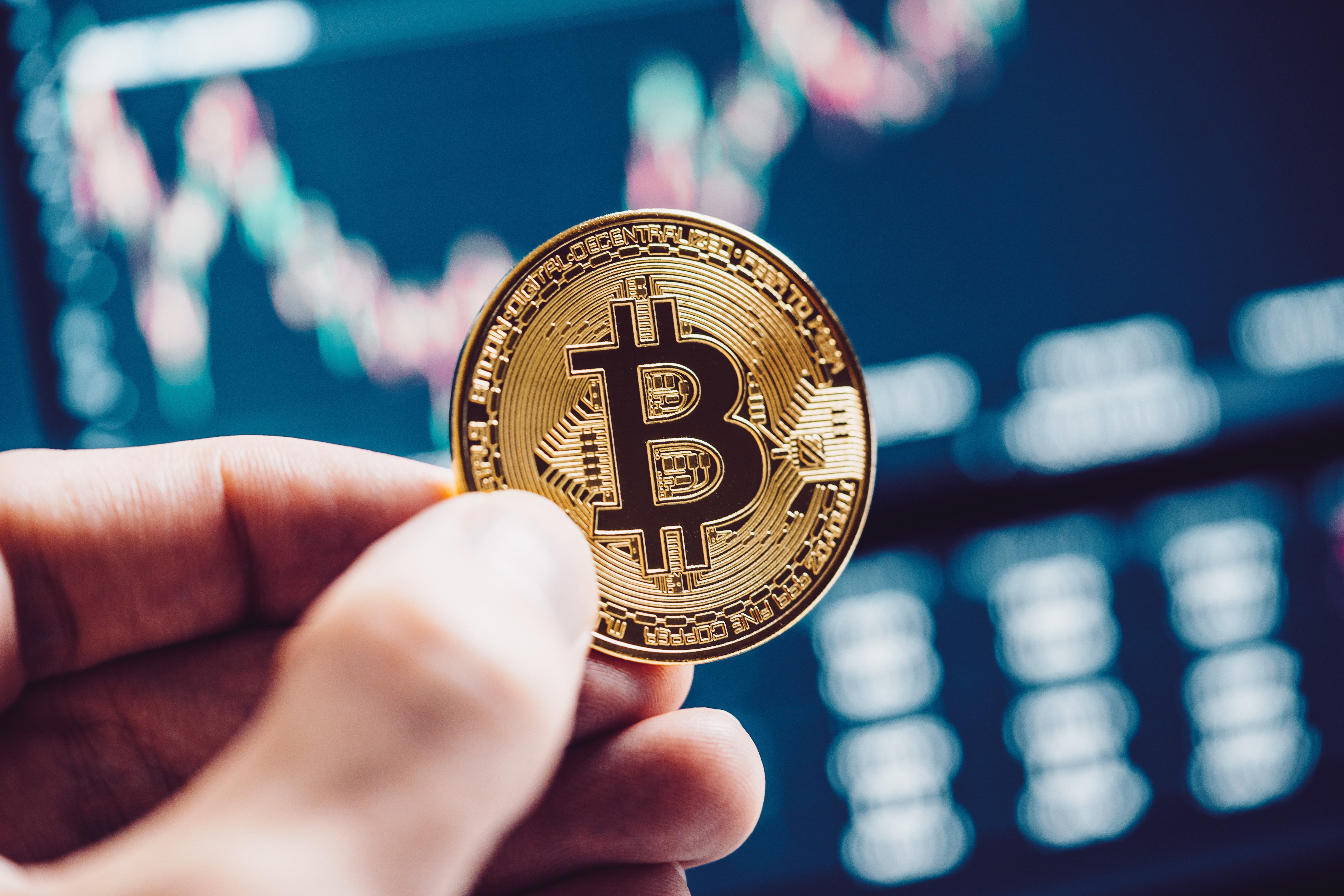 Bitcoin coin held in hand with stock chart background HD Wallpaper