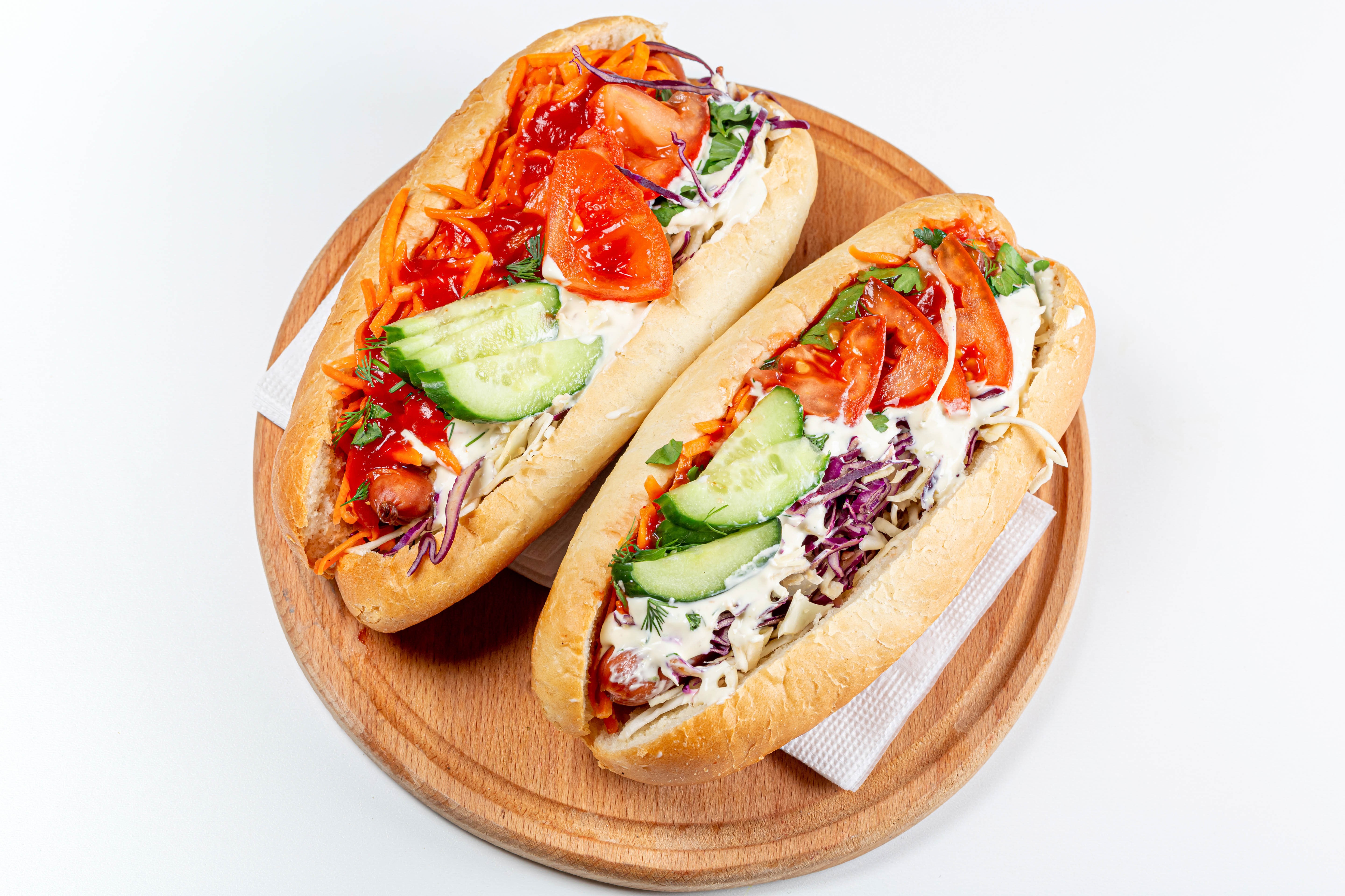 Two hot dogs with vegetables on a cutting board HD Wallpaper