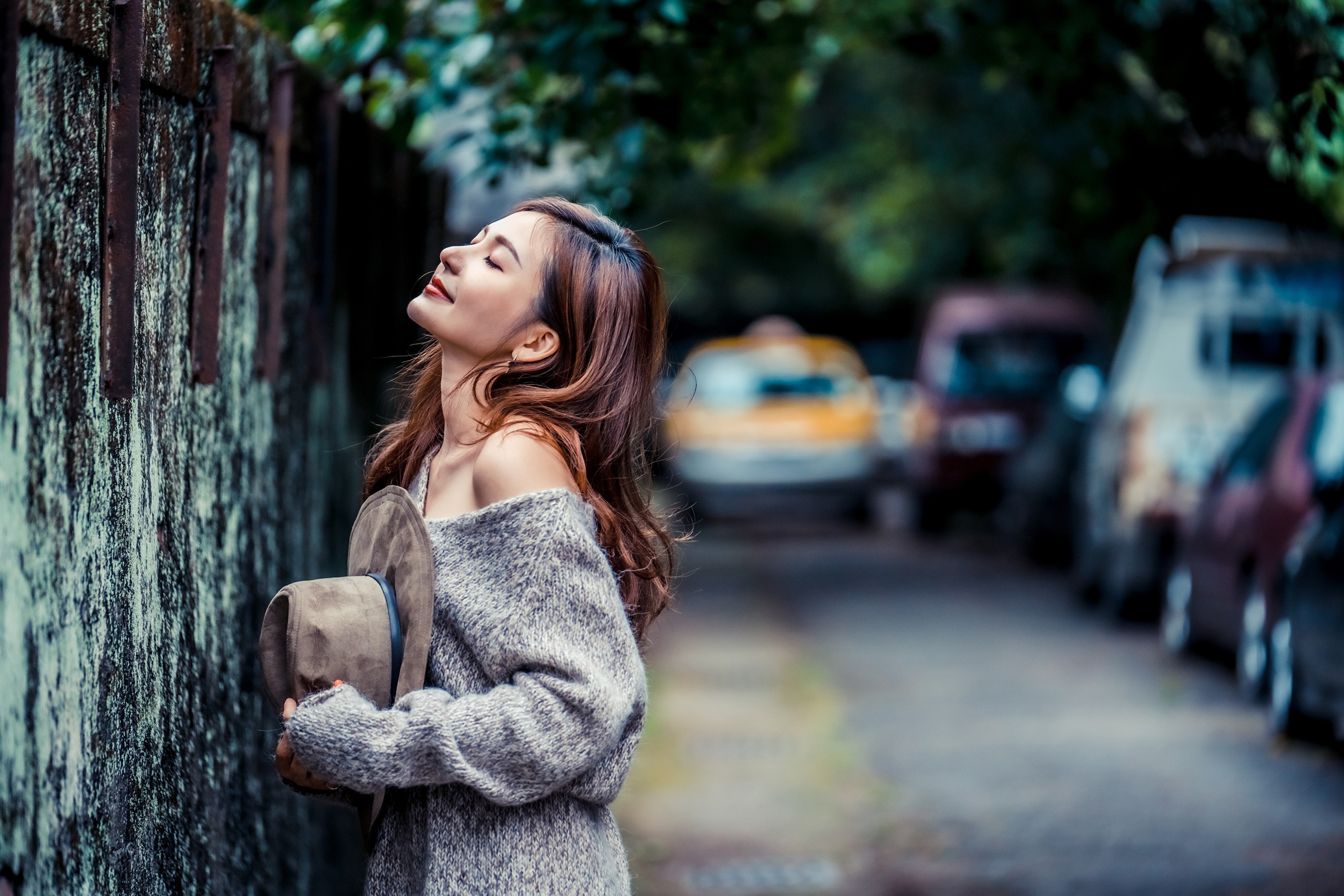 Asian woman in sweater holding hat, posing by wall HD Wallpaper