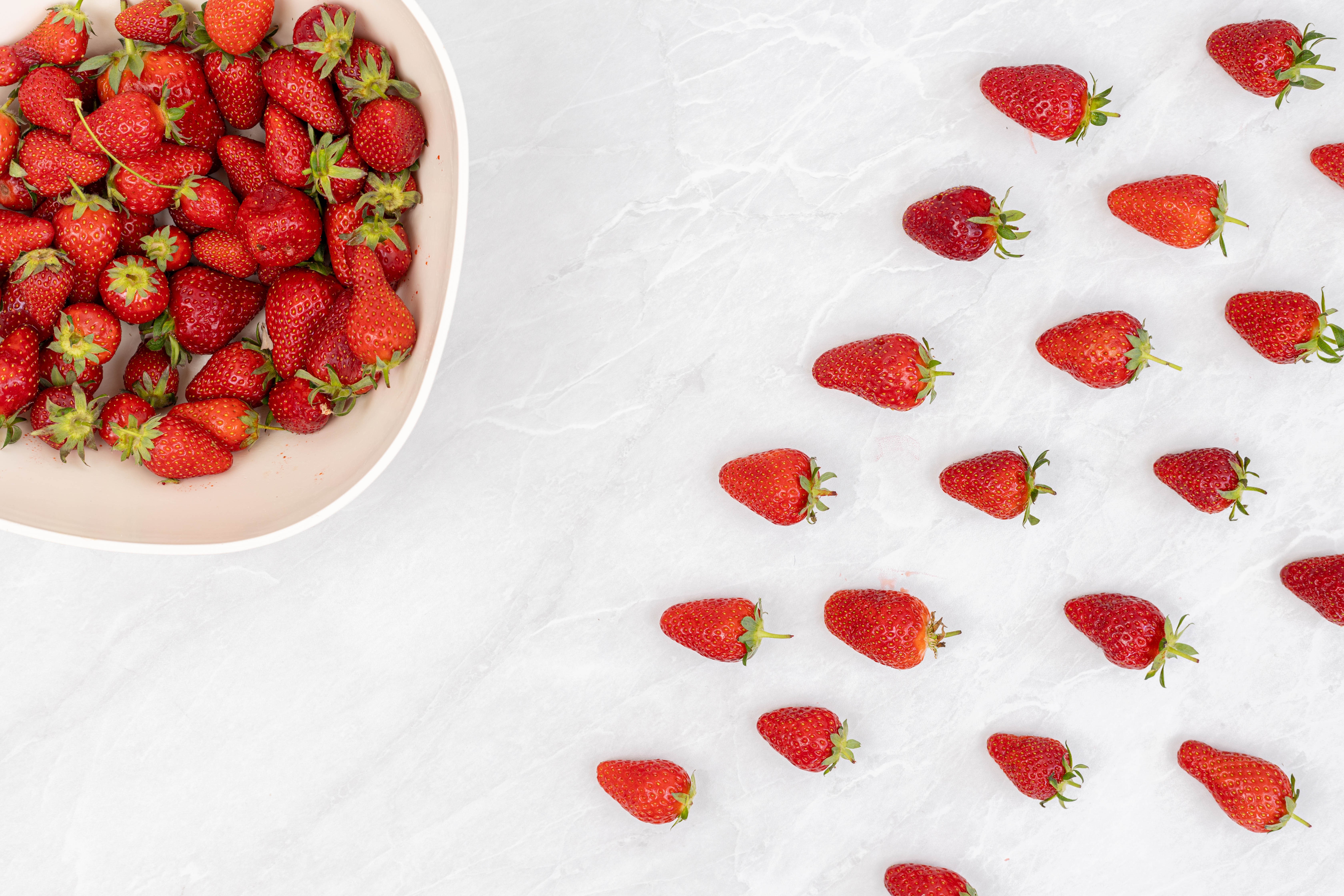 Strawberries in a bowl and scattered on a white background HD Wallpaper
