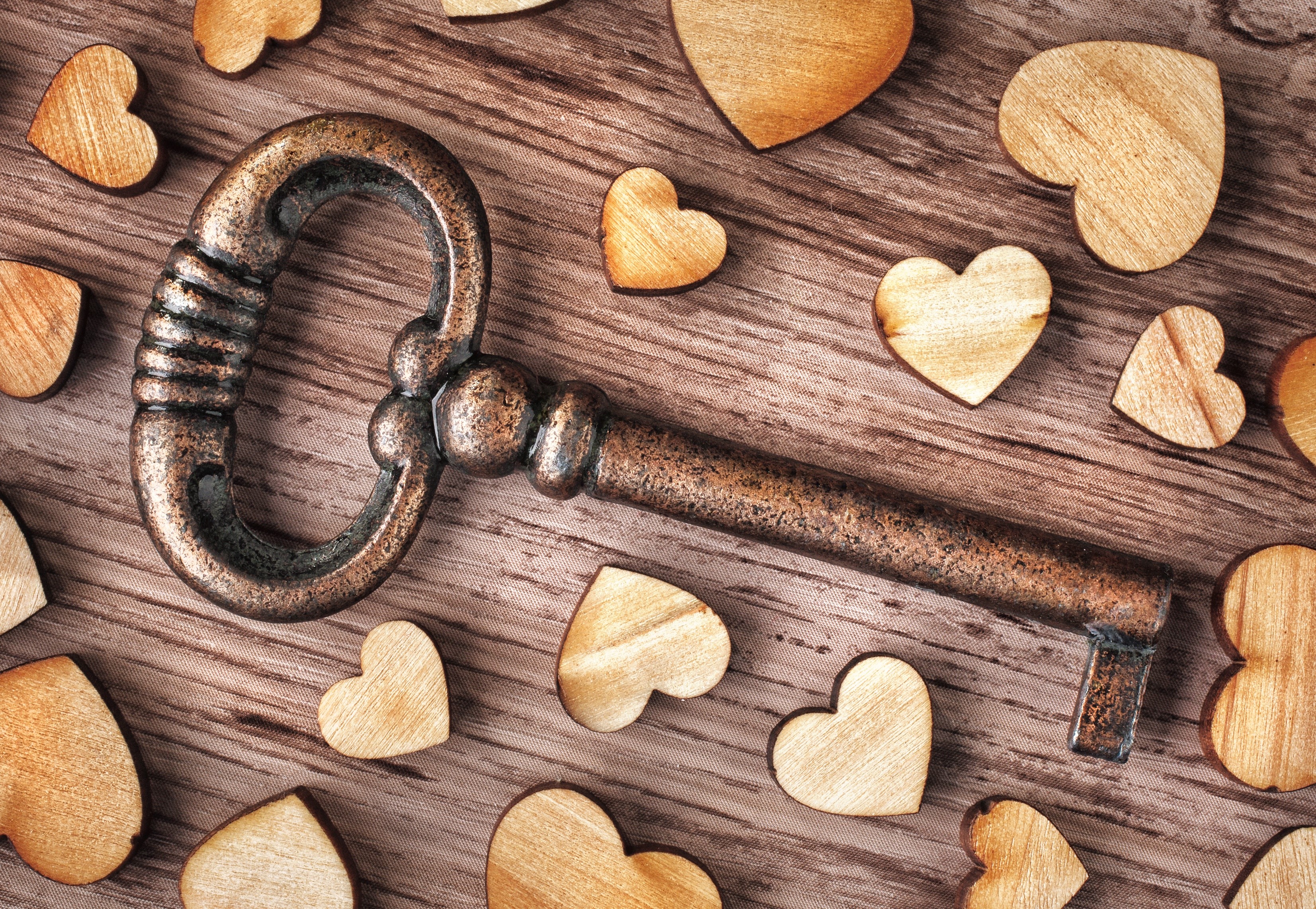 Antique key surrounded by wooden hearts on a wooden surface HD Wallpaper