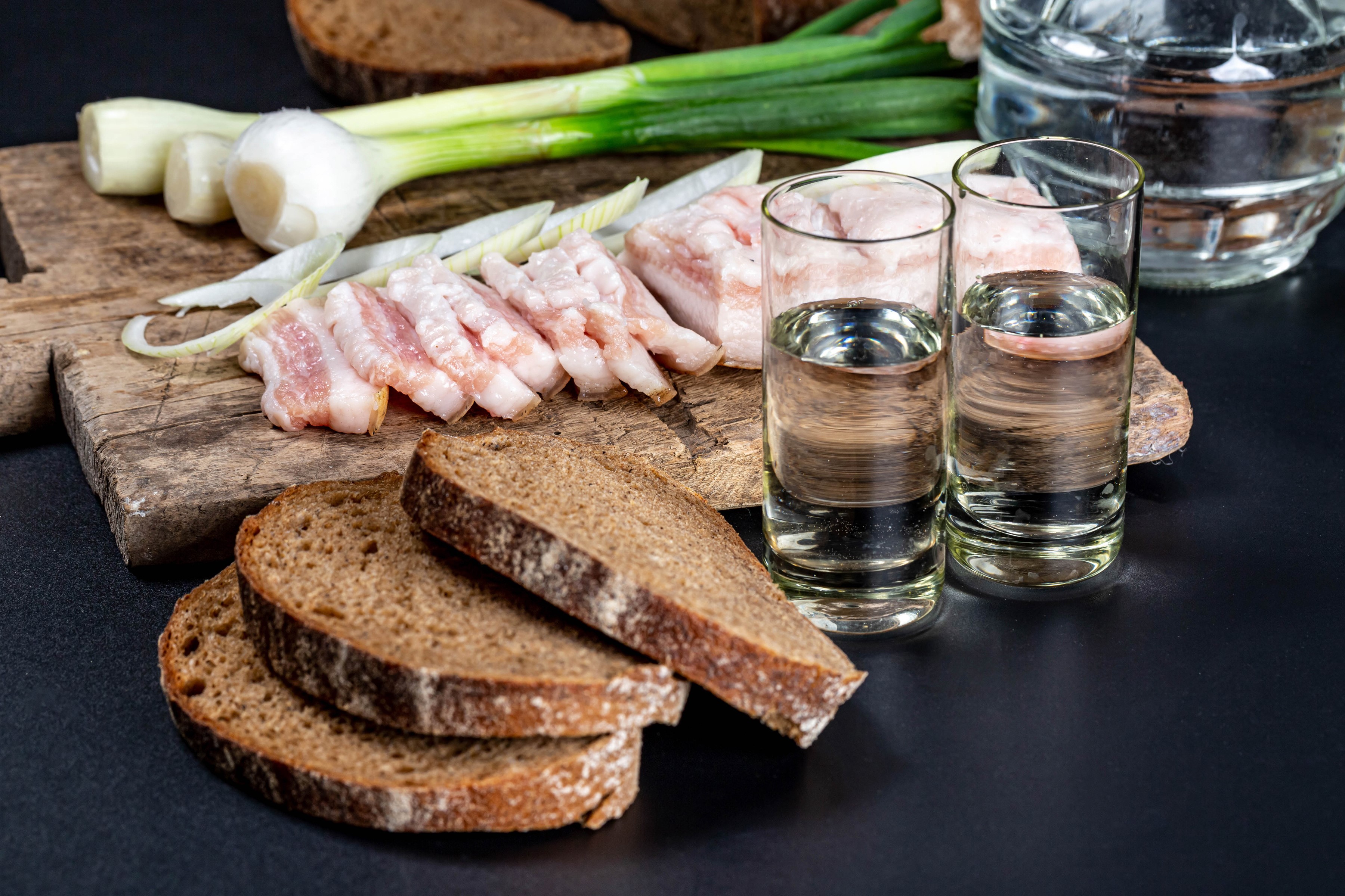 Salo, scallions, bread, and vodka shots on a cutting board HD Wallpaper
