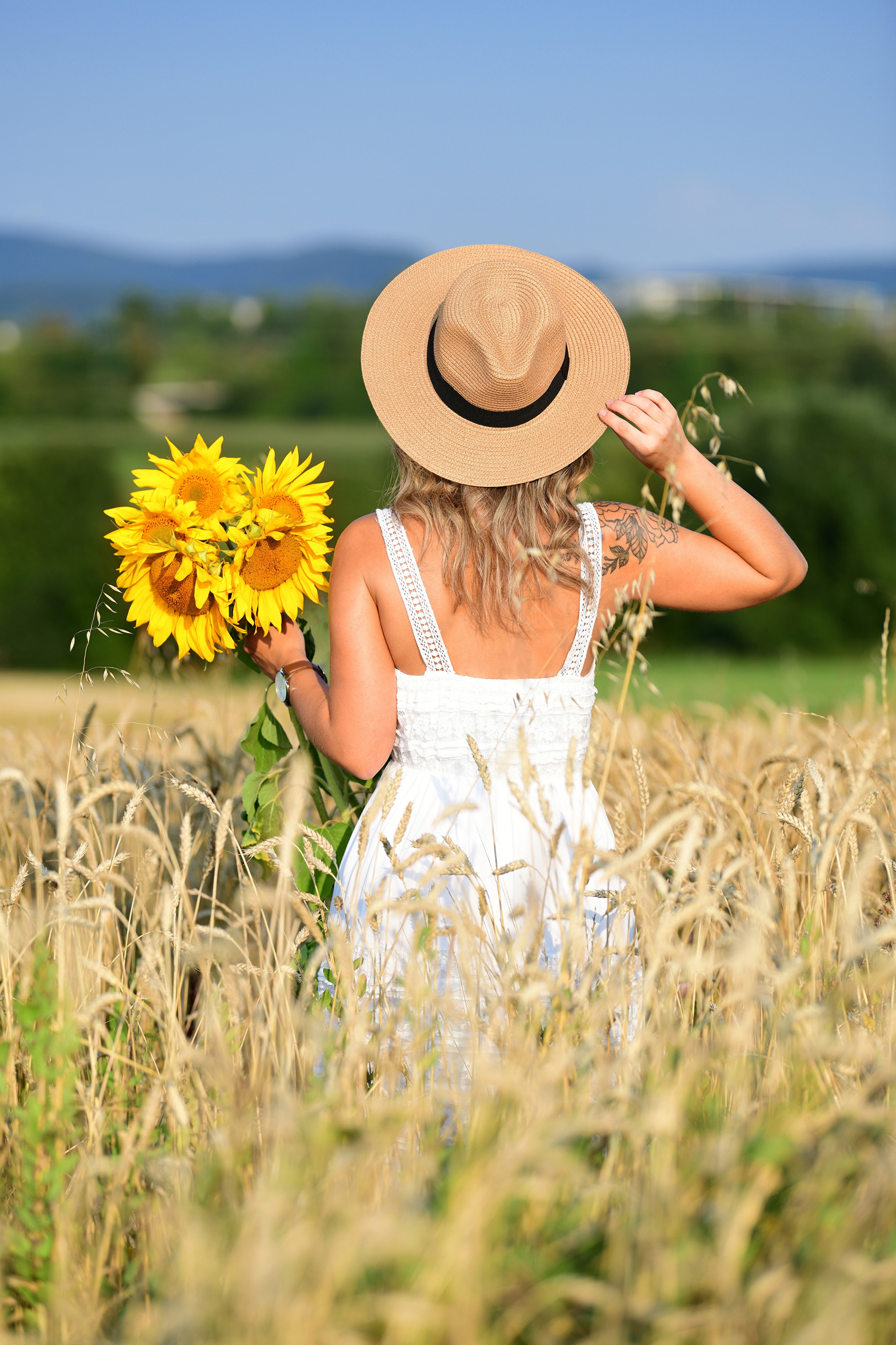 Woman in white dress holding sunflowers in a wheat field HD Phone Wallpaper