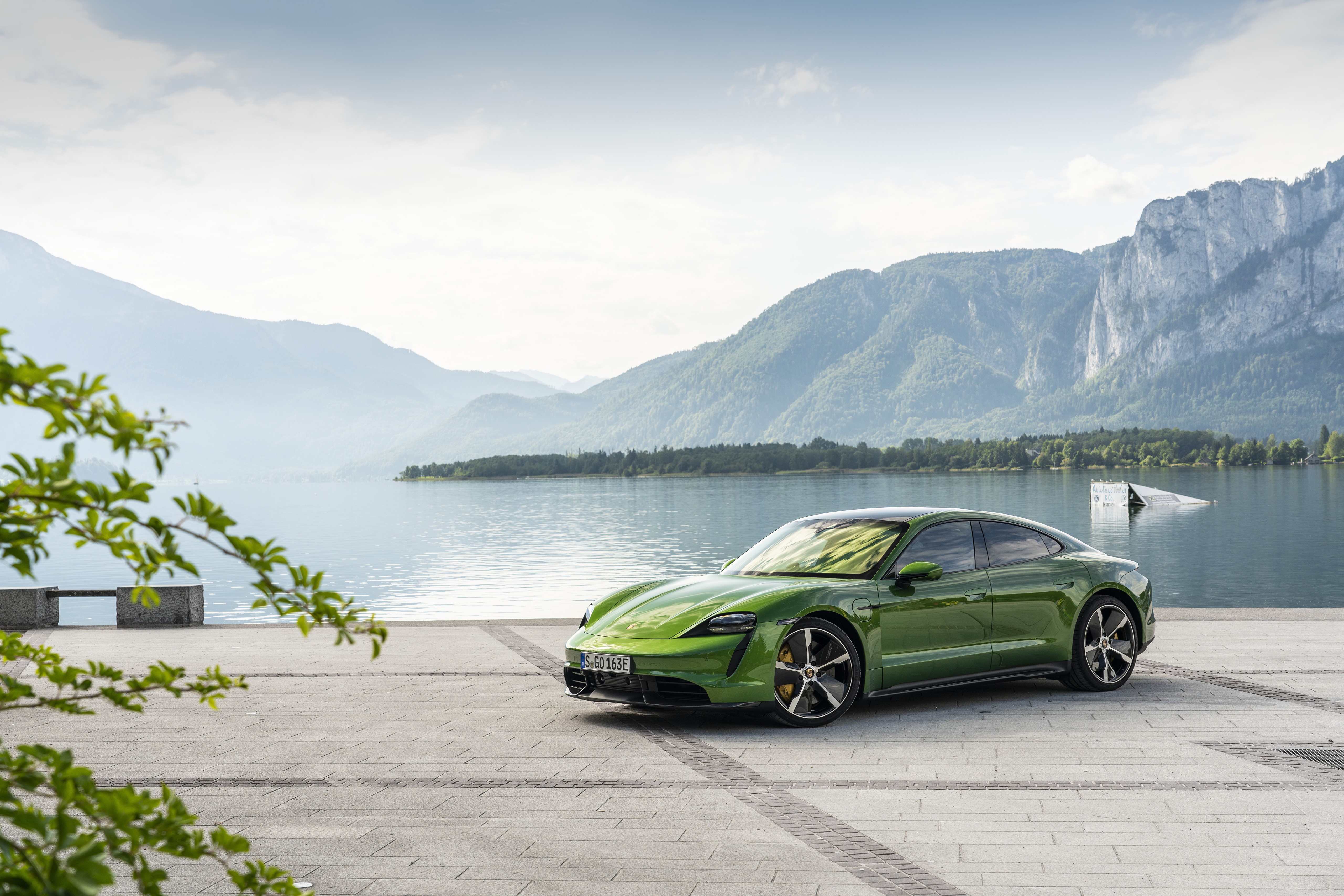Green Porsche Taycan by a lake with mountains HD Wallpaper