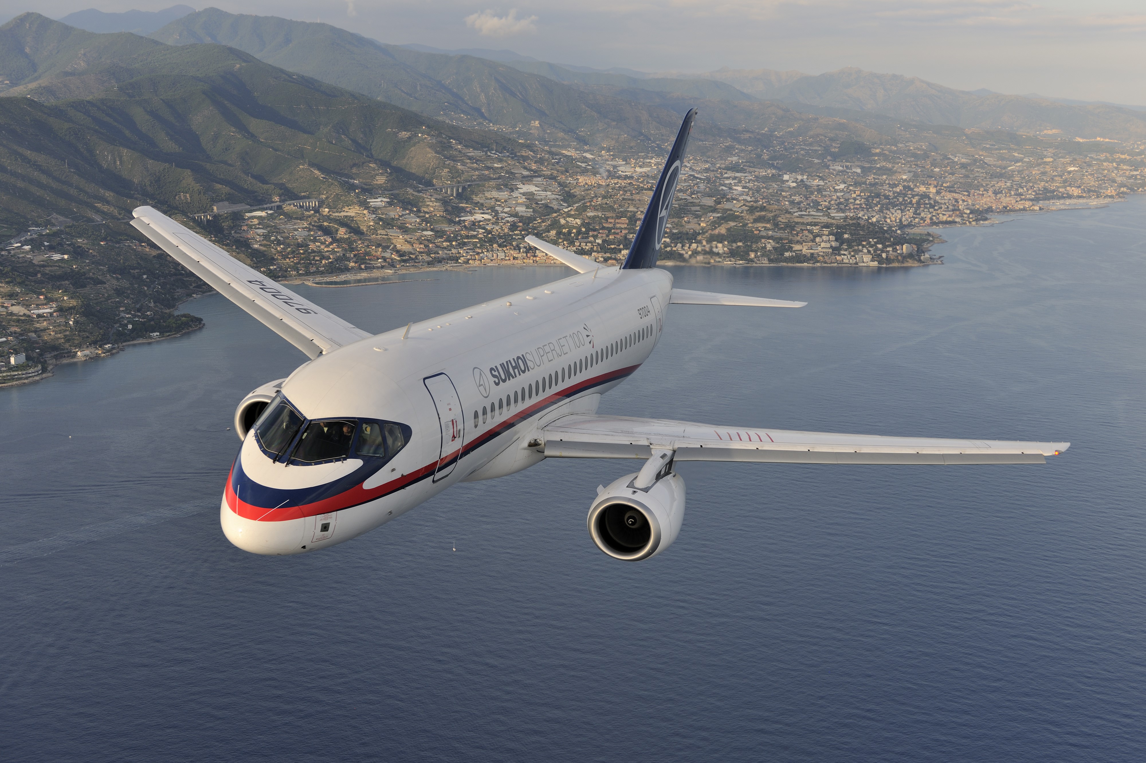Sukhoi Superjet 100 flying over a coastal city HD Wallpaper