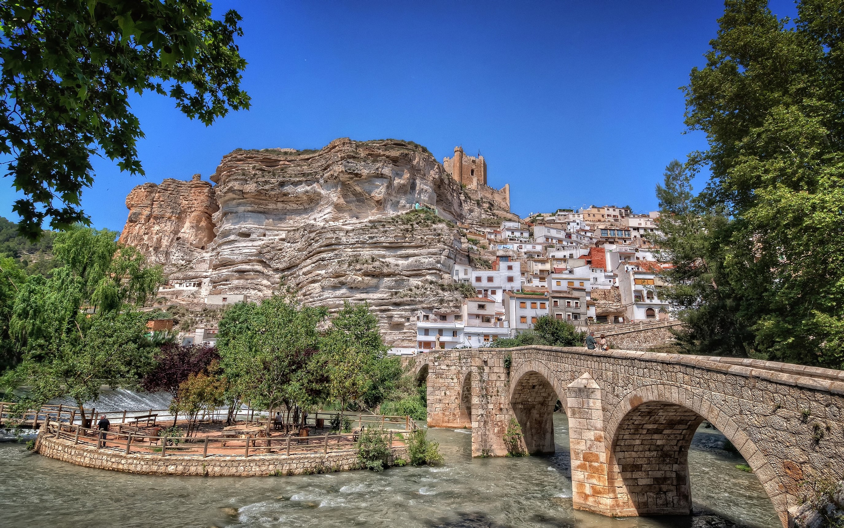 Town built on a cliffside with a stone bridge over a river HD Wallpaper