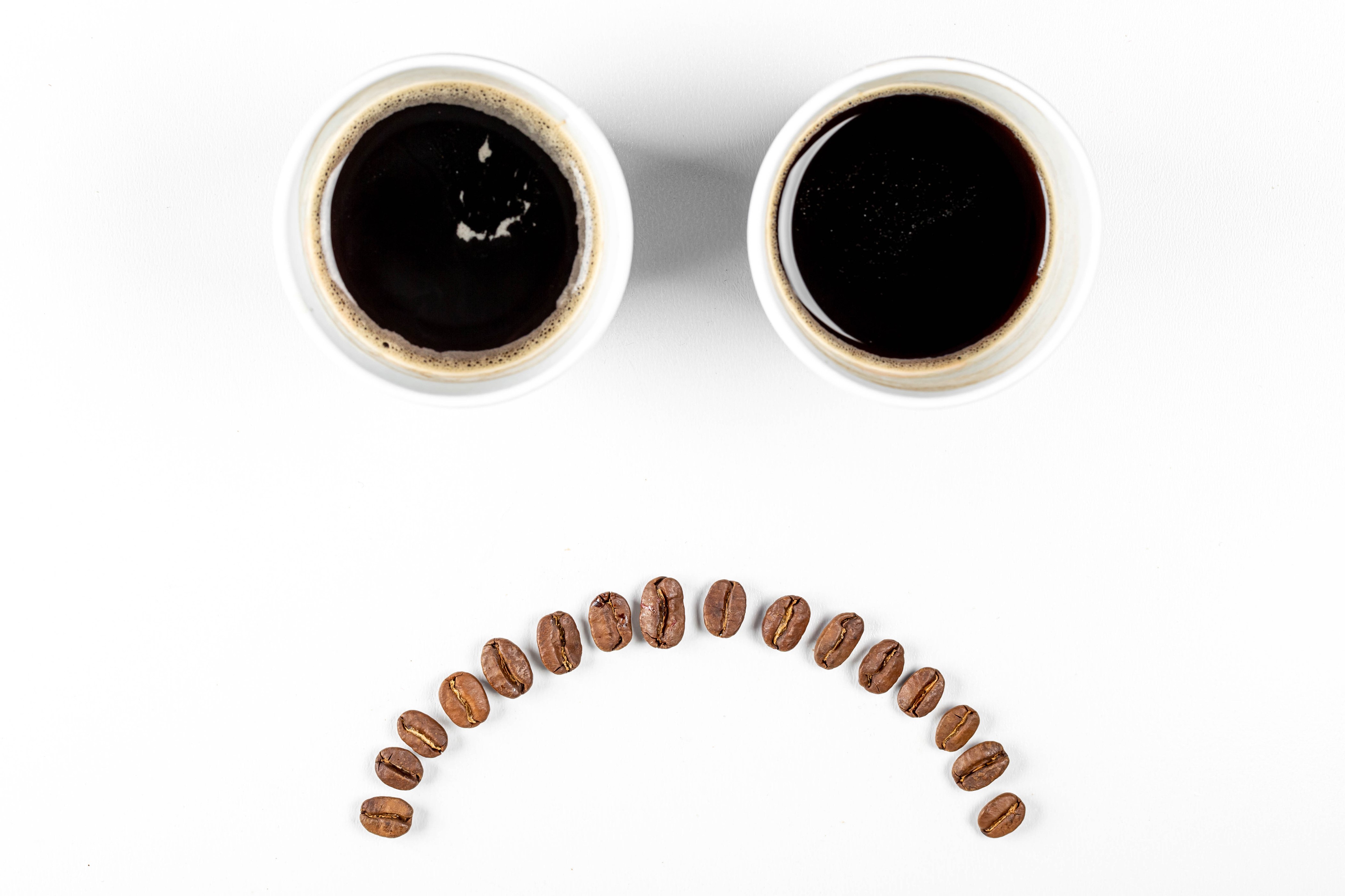 Two cups of coffee and coffee beans forming a sad face HD Wallpaper
