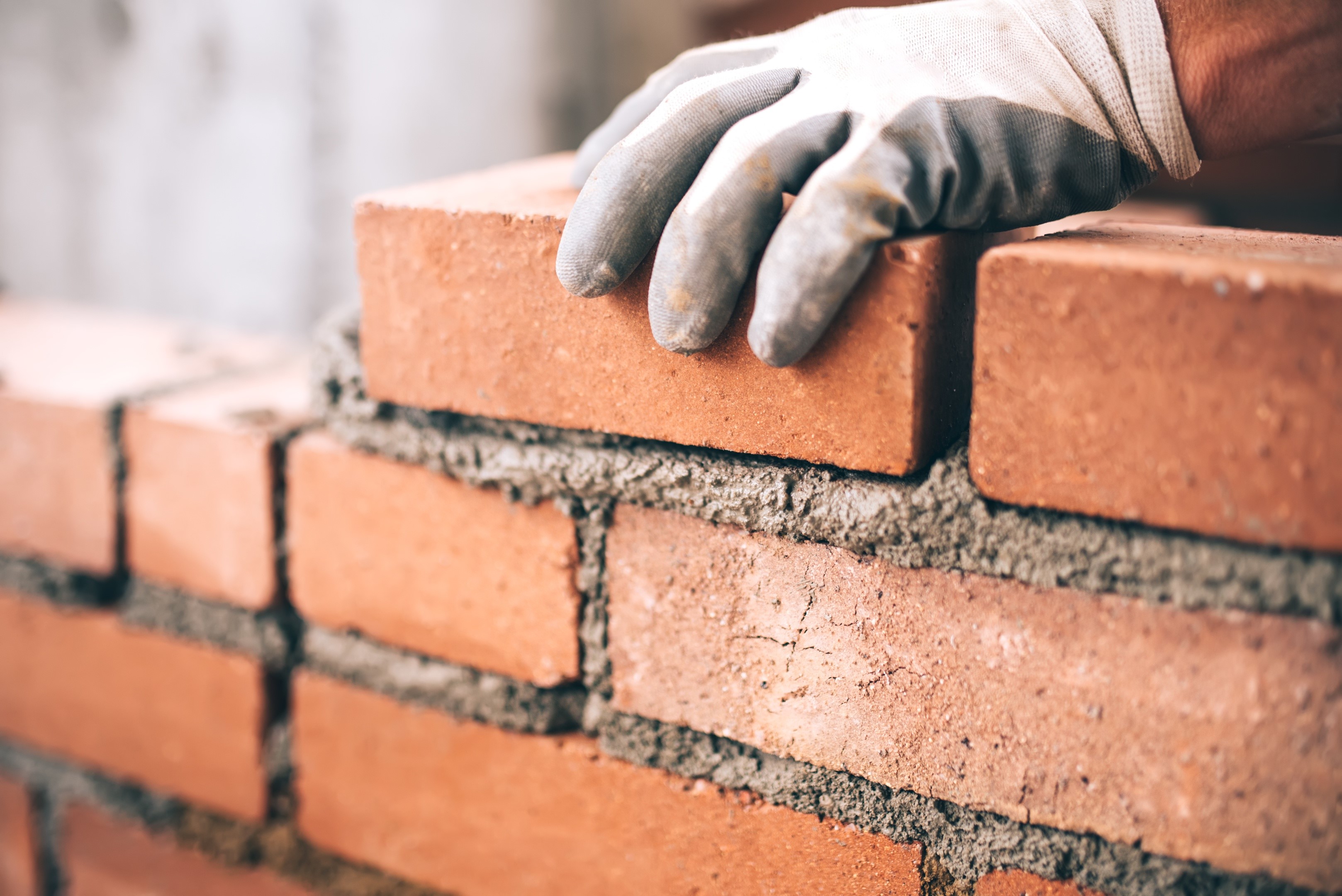 Bricklayer's gloved hand placing a brick on a wall HD Wallpaper