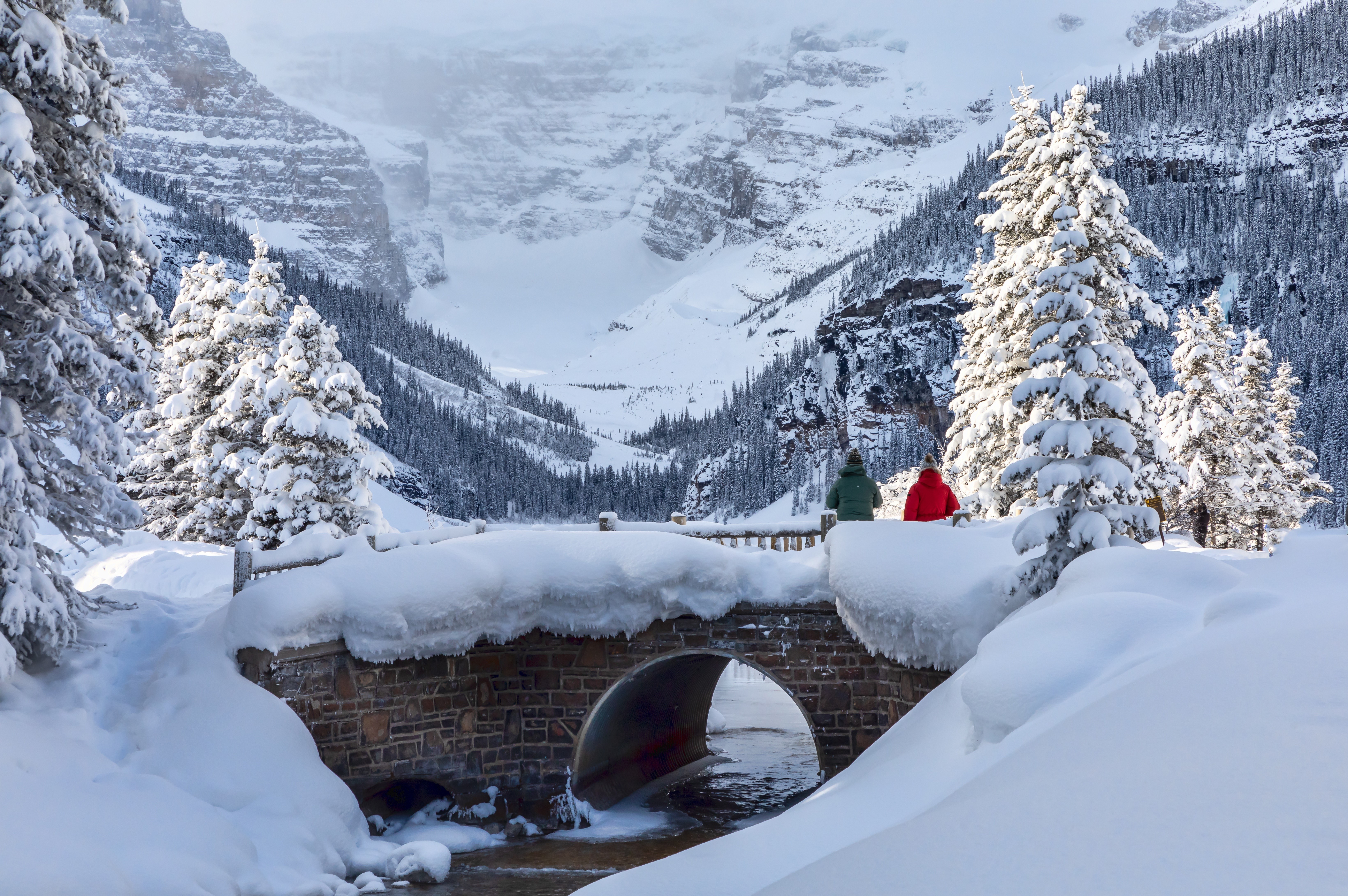 Snowy bridge over stream with mountains and trees in Banff HD Wallpaper