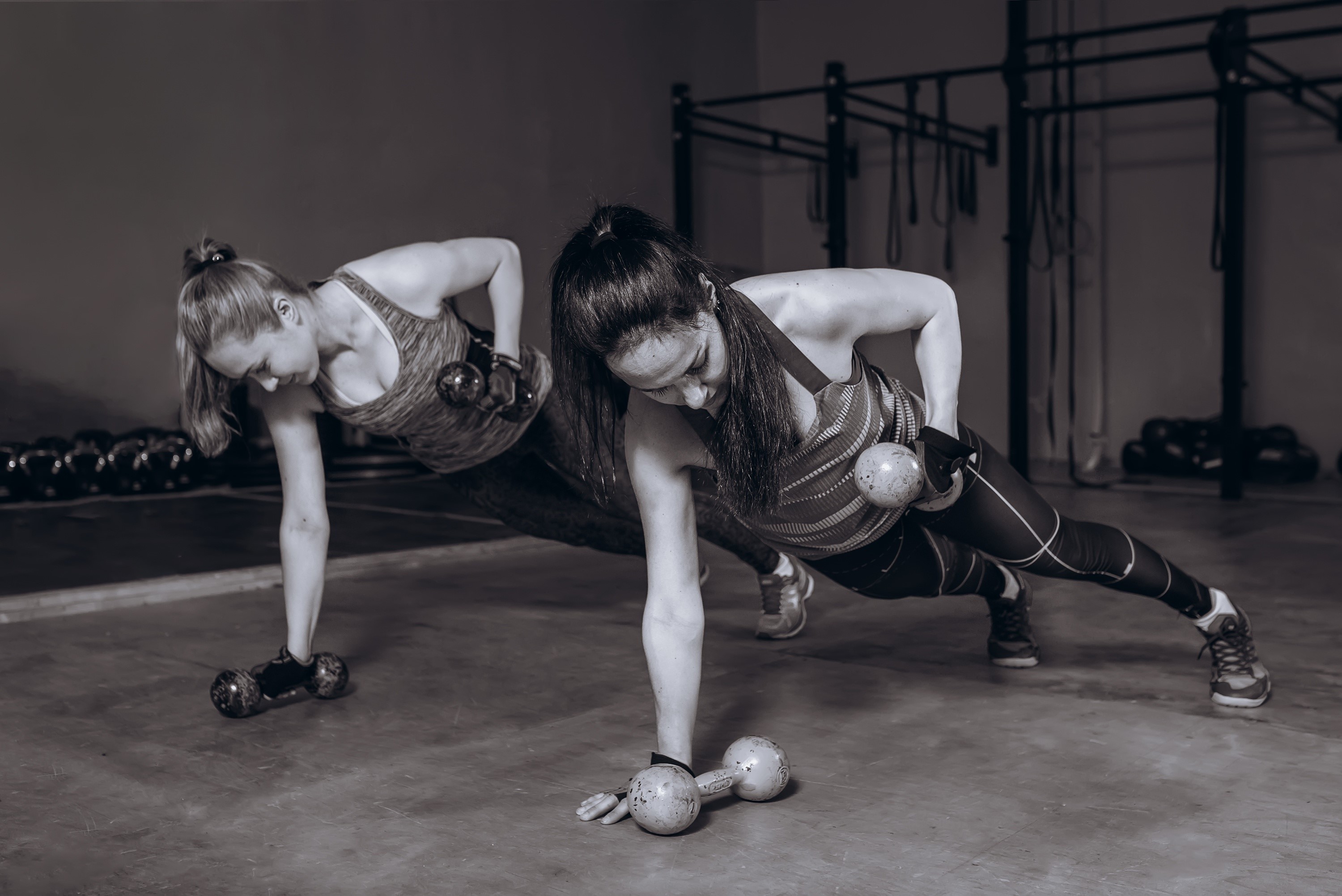 Two women doing dumbbell plank exercise in gym HD Wallpaper