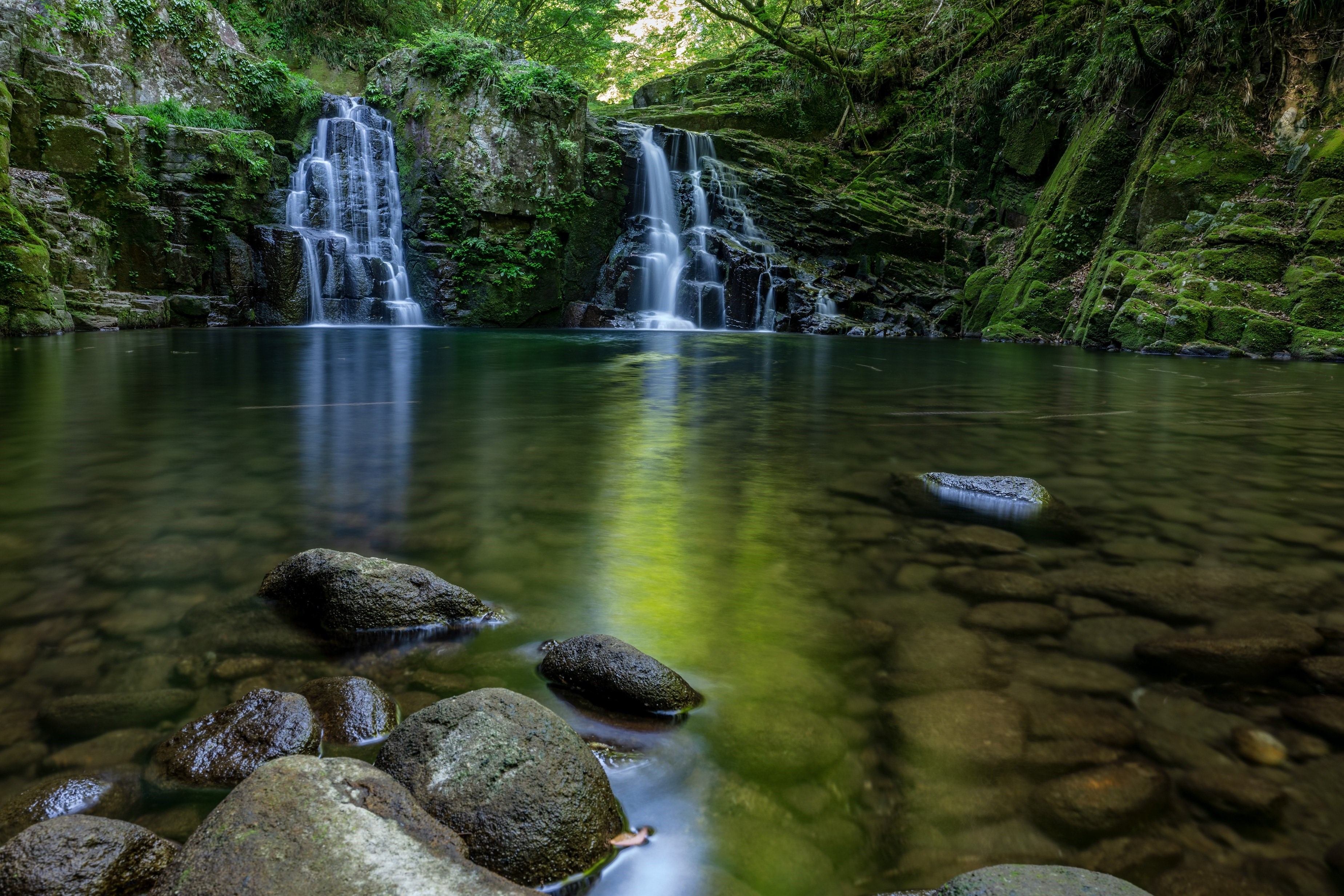 Waterfalls cascading into a clear pool surrounded by mossy rocks HD Wallpaper