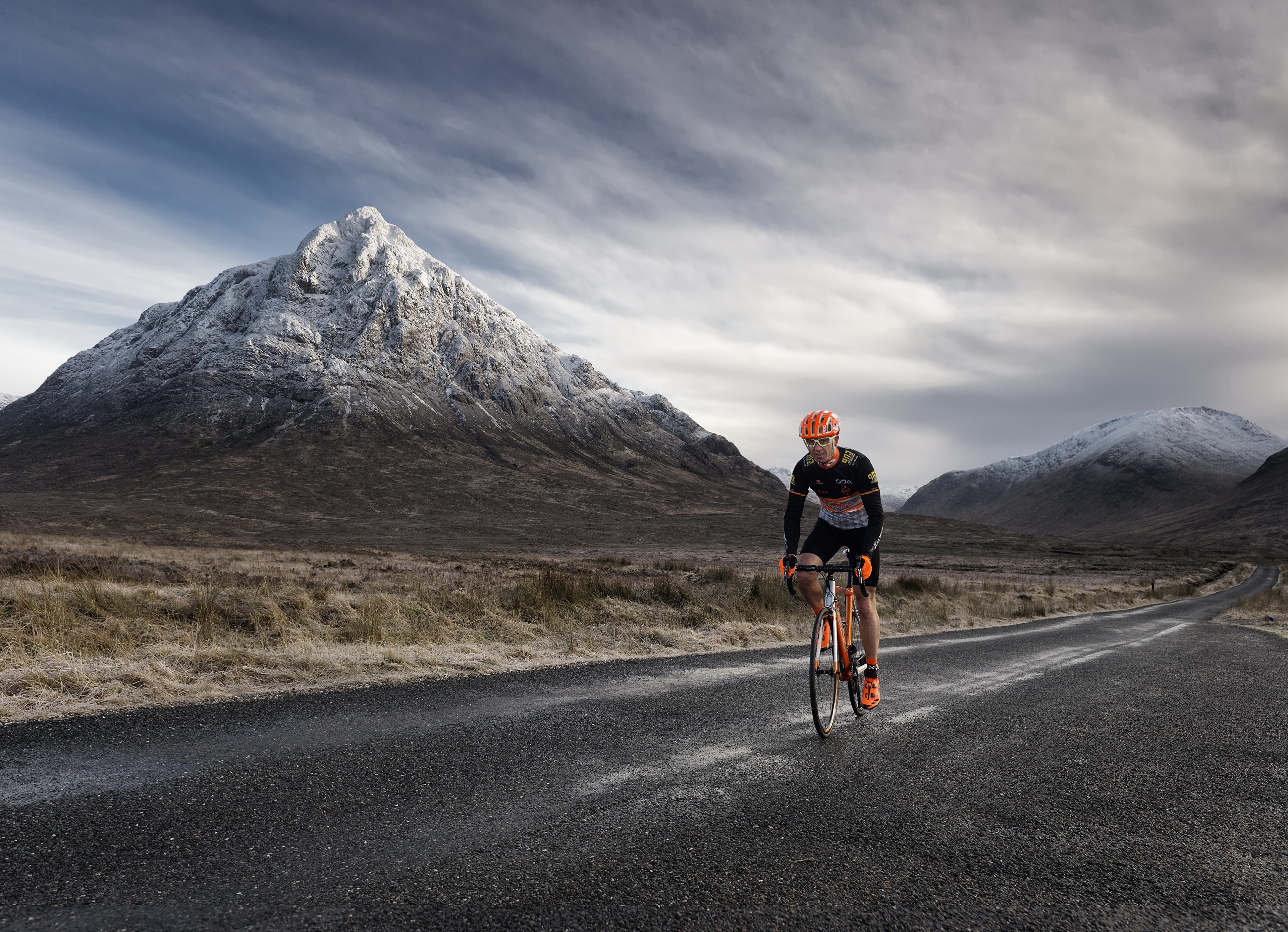 Cyclist on a road with snow-capped mountains HD Wallpaper