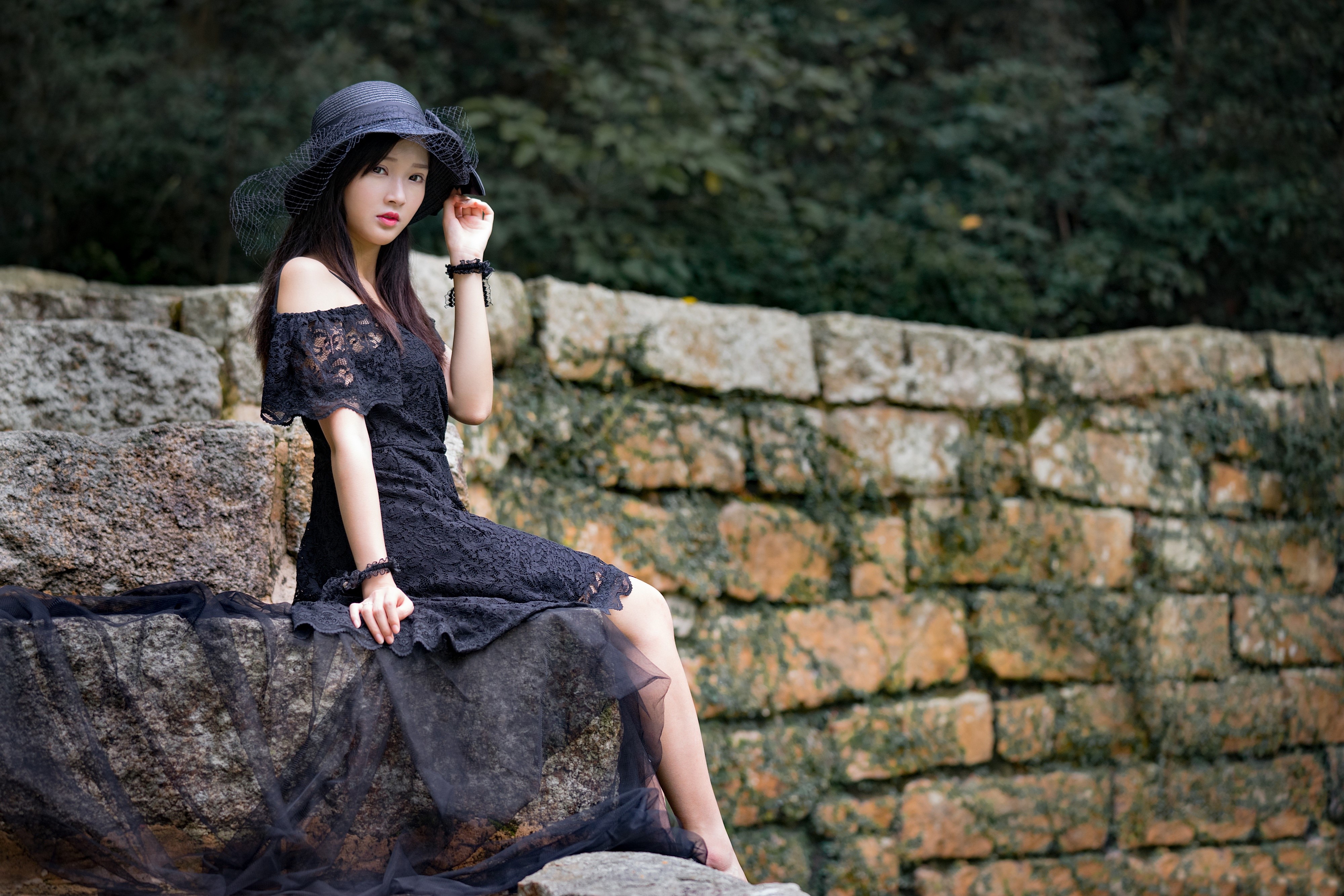 Brunette girl in black dress and hat sitting on rocks HD Wallpaper