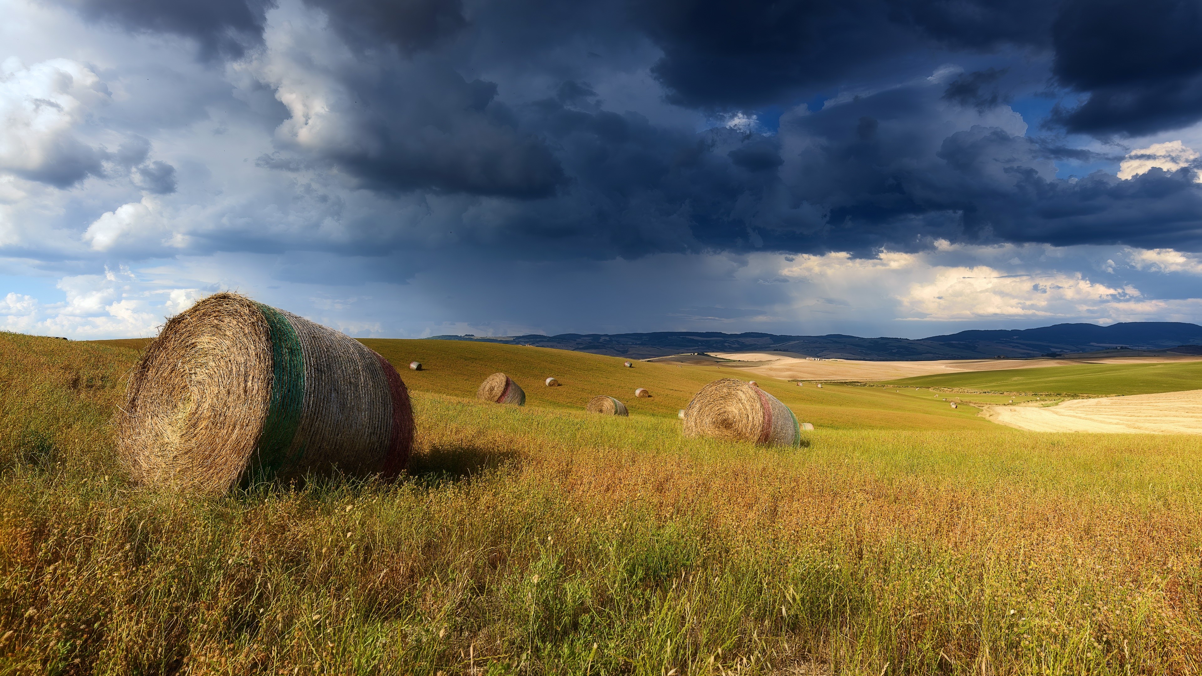 Hay bales in a field under thunderclouds HD Wallpaper