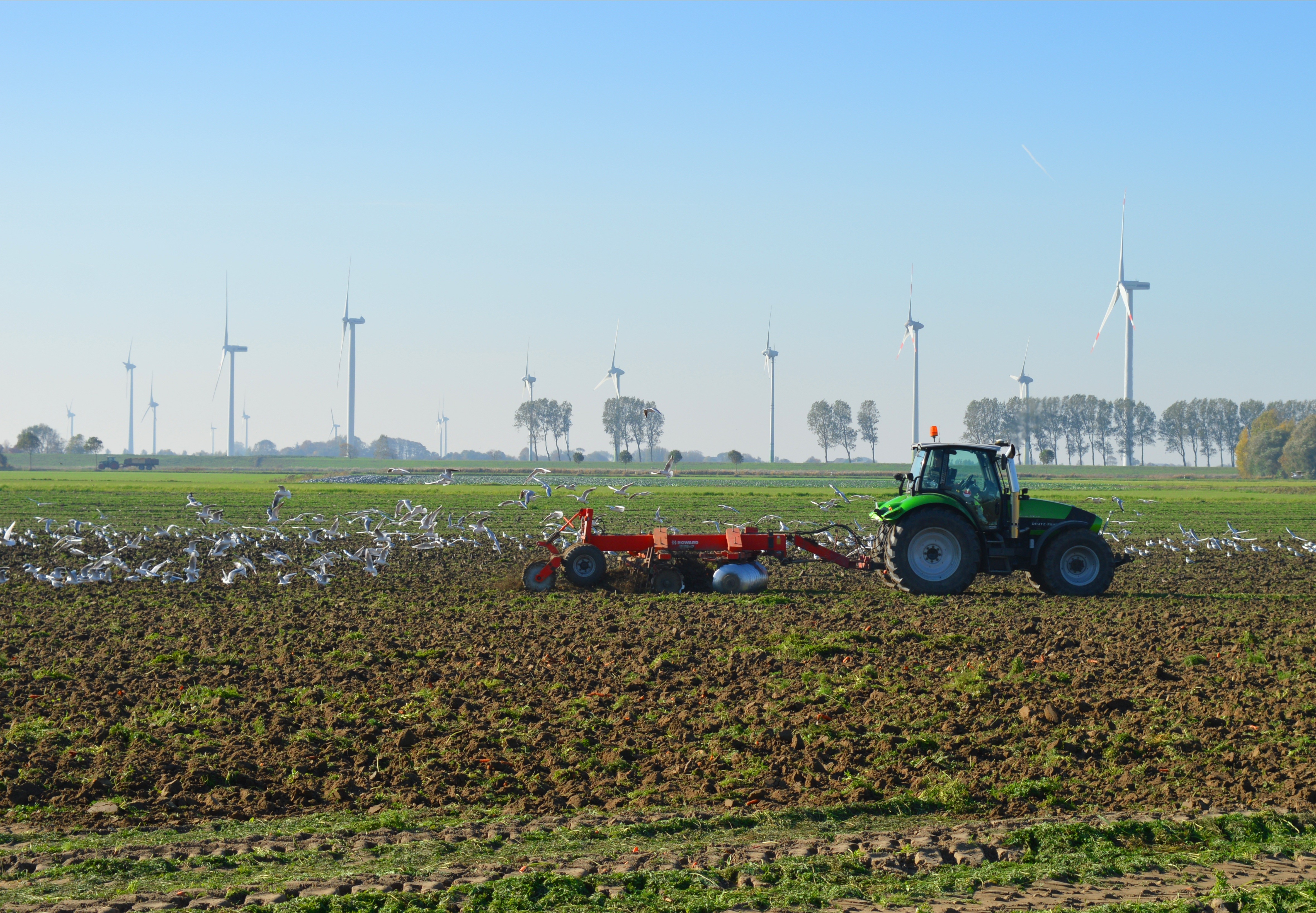 Tractor plowing a field with birds and wind turbines HD Wallpaper