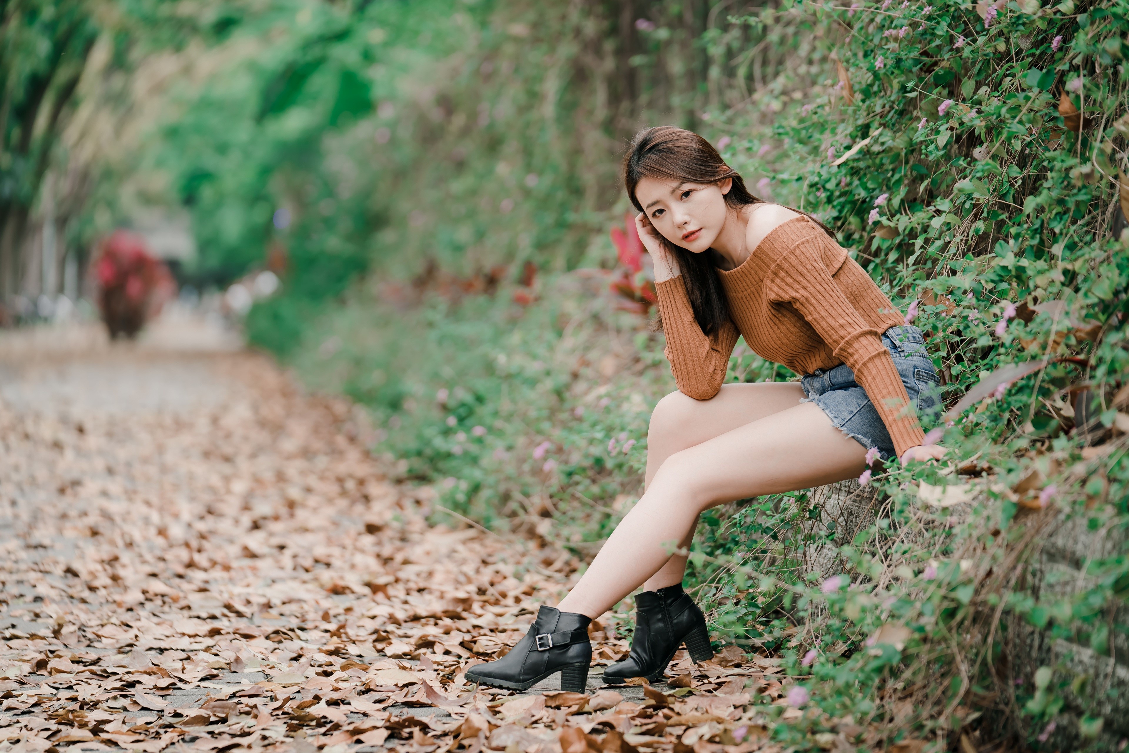 Asian woman with brown hair sitting on a path covered in leaves HD Wallpaper