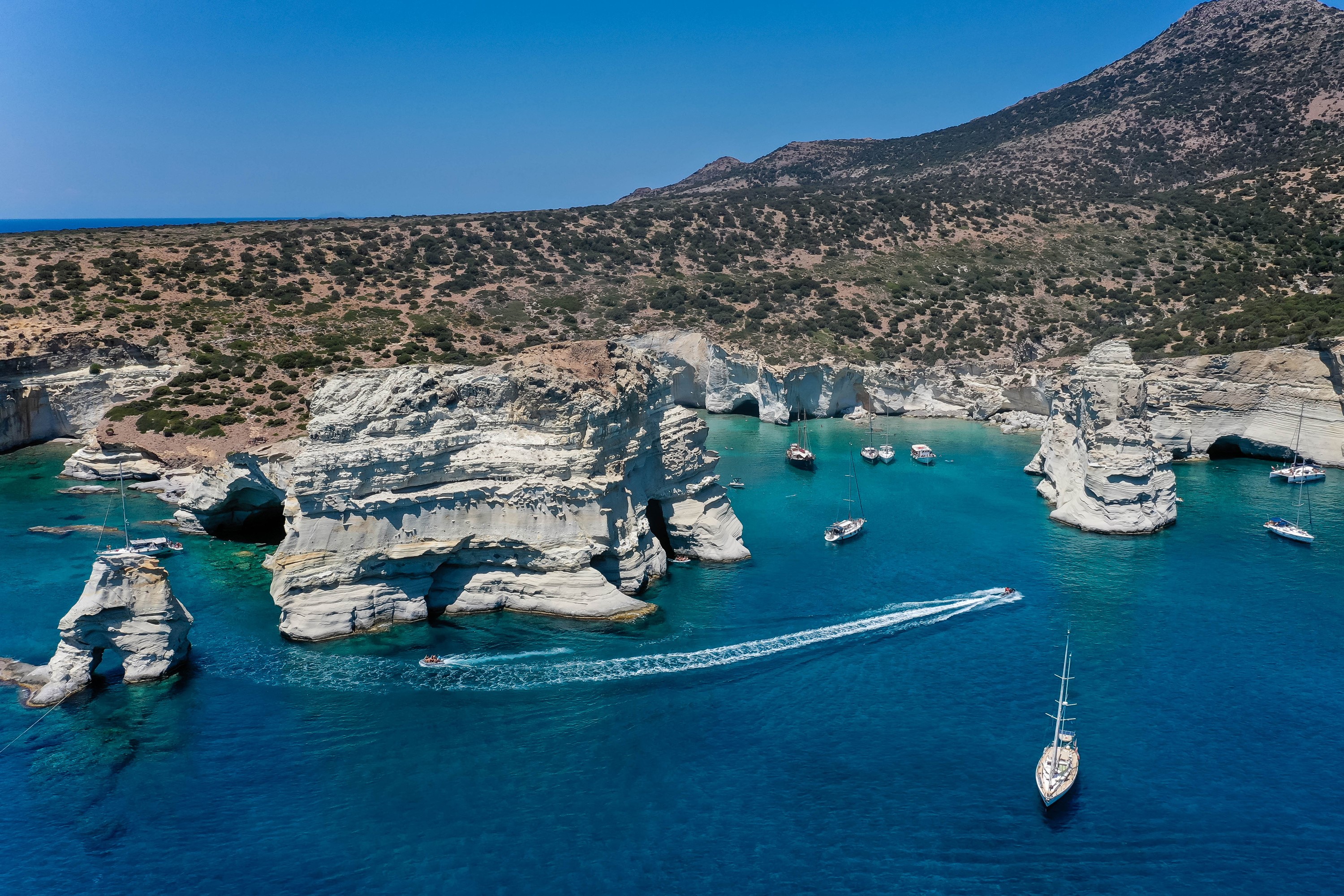Boats in a cove with white cliffs on Milos, Greece HD Wallpaper