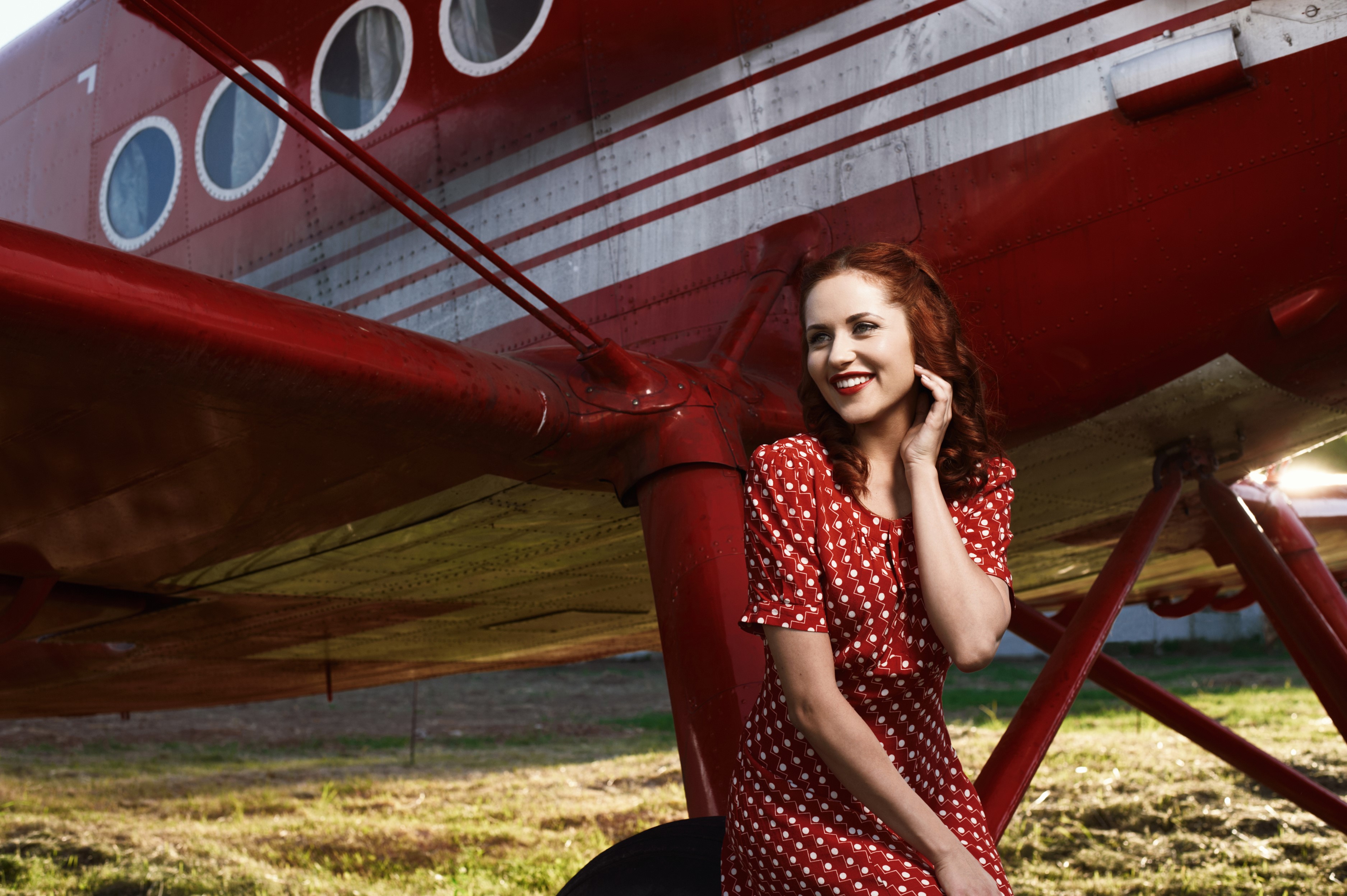 Redhead woman in polka dot dress posing by a red airplane HD Wallpaper