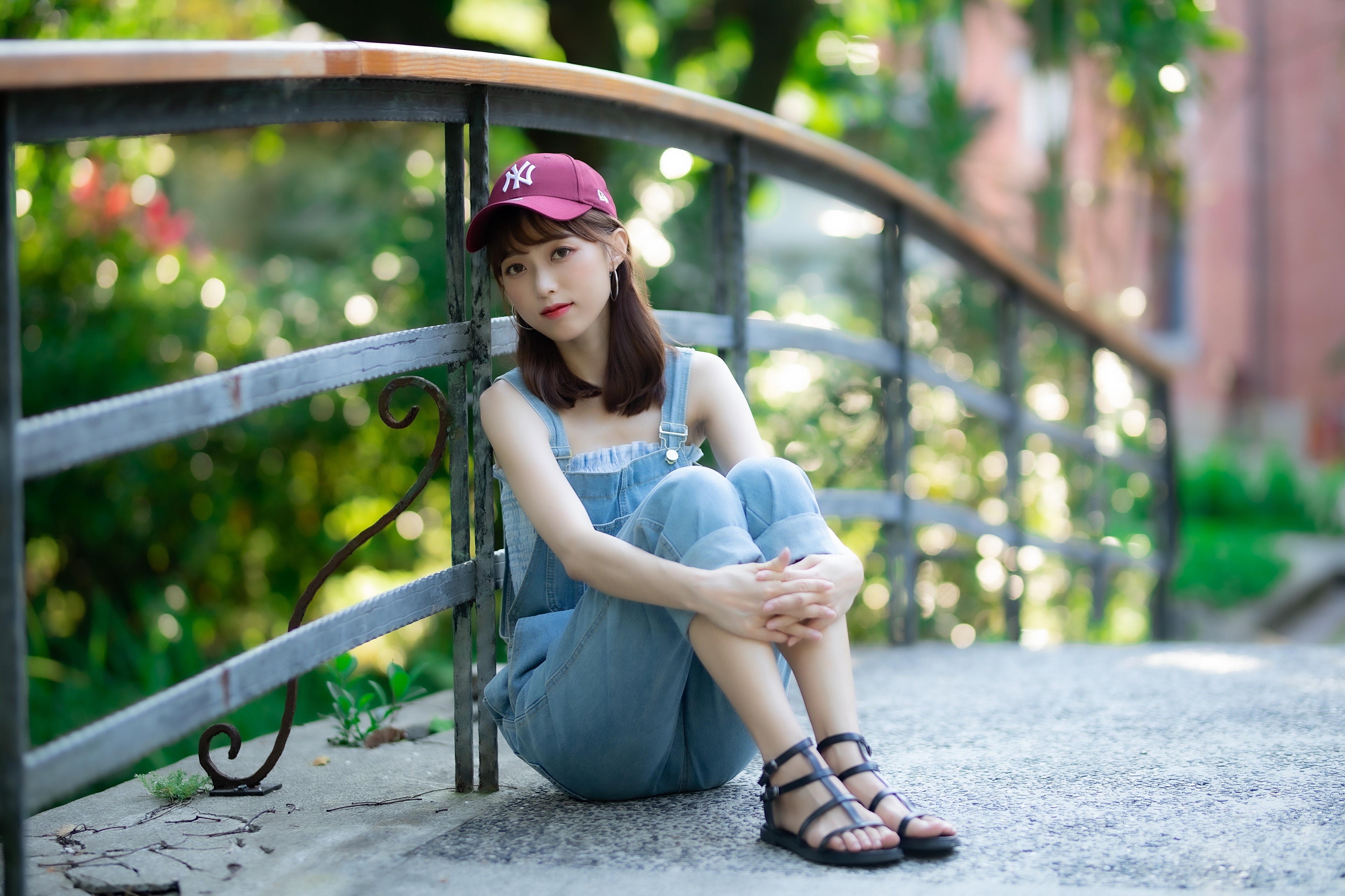 Asian girl in baseball cap and overalls sitting on bridge HD Wallpaper