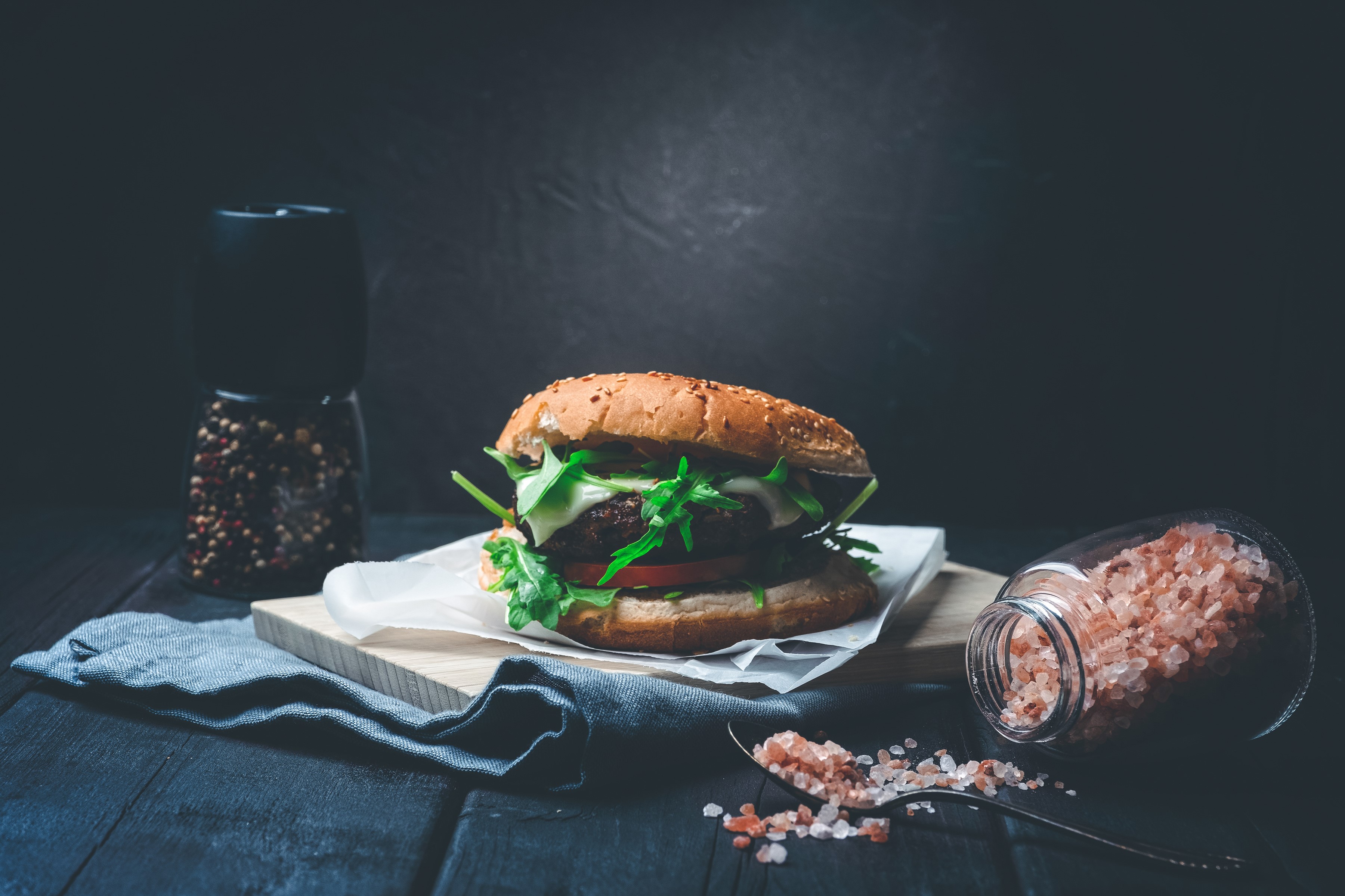 Hamburger with salt and pepper shakers on wooden table HD Wallpaper