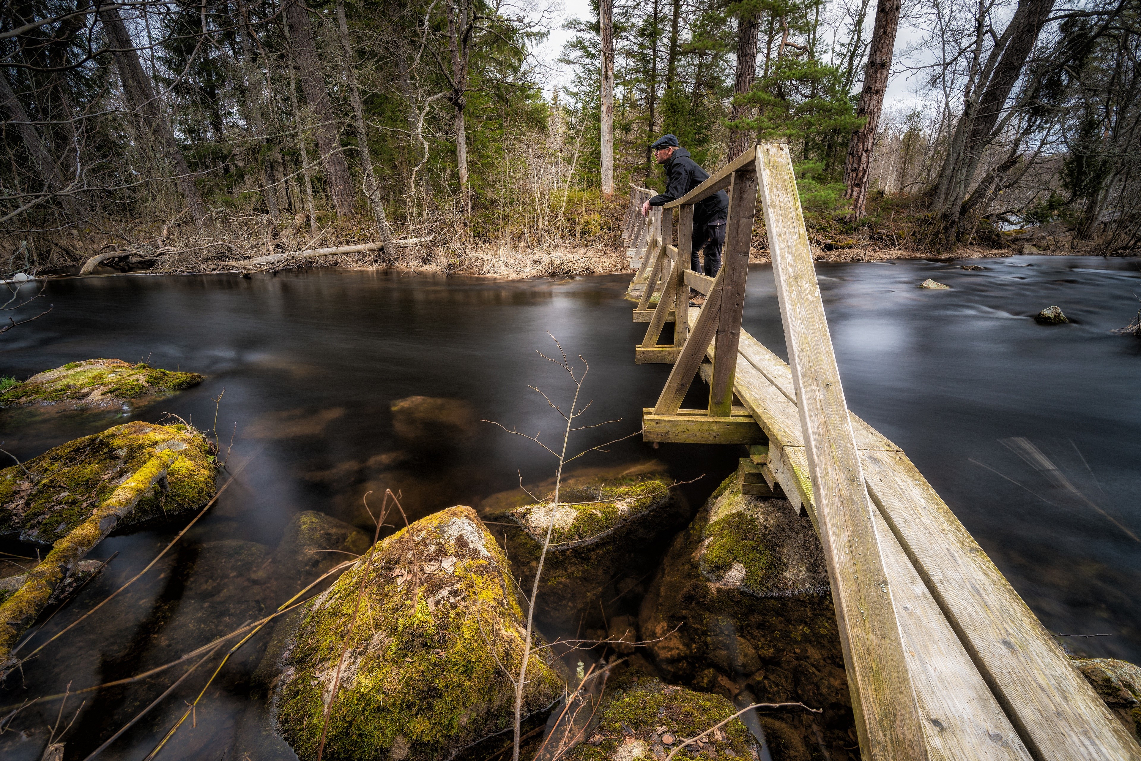 Man on a wooden bridge over a river with stones HD Wallpaper