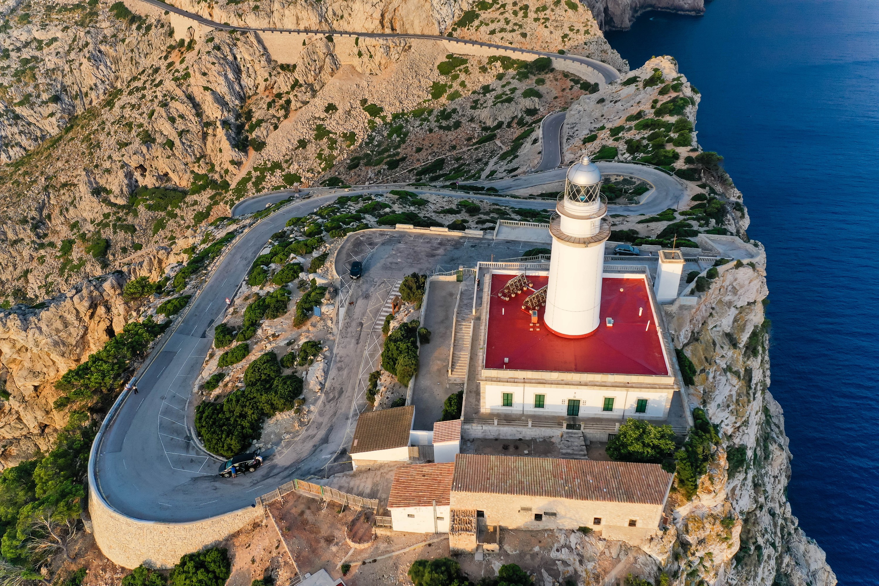 Lighthouse on a cliff with winding road in Mallorca, Spain HD Wallpaper