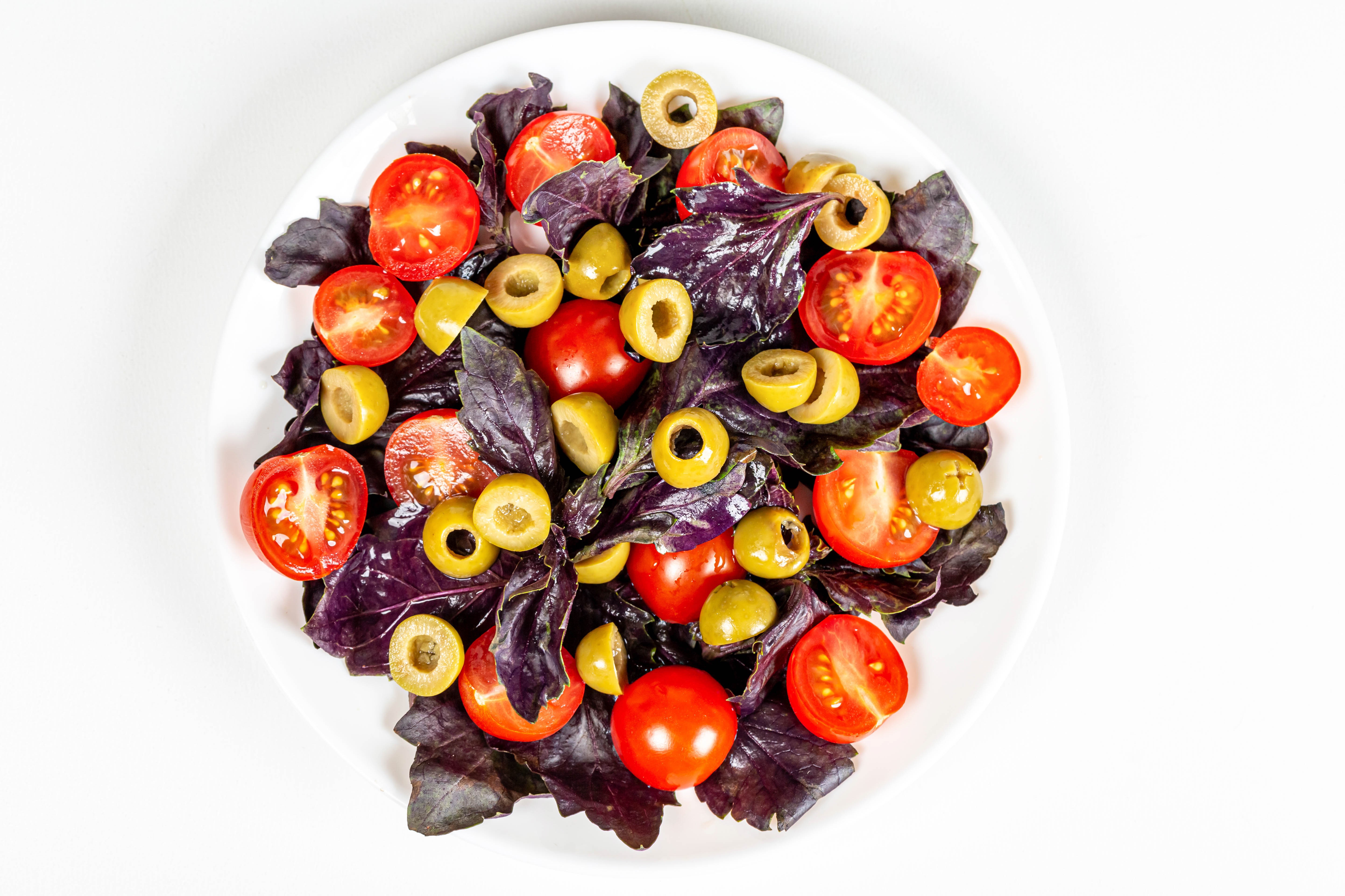 Salad with tomatoes, olives, and basil on a white plate HD Wallpaper