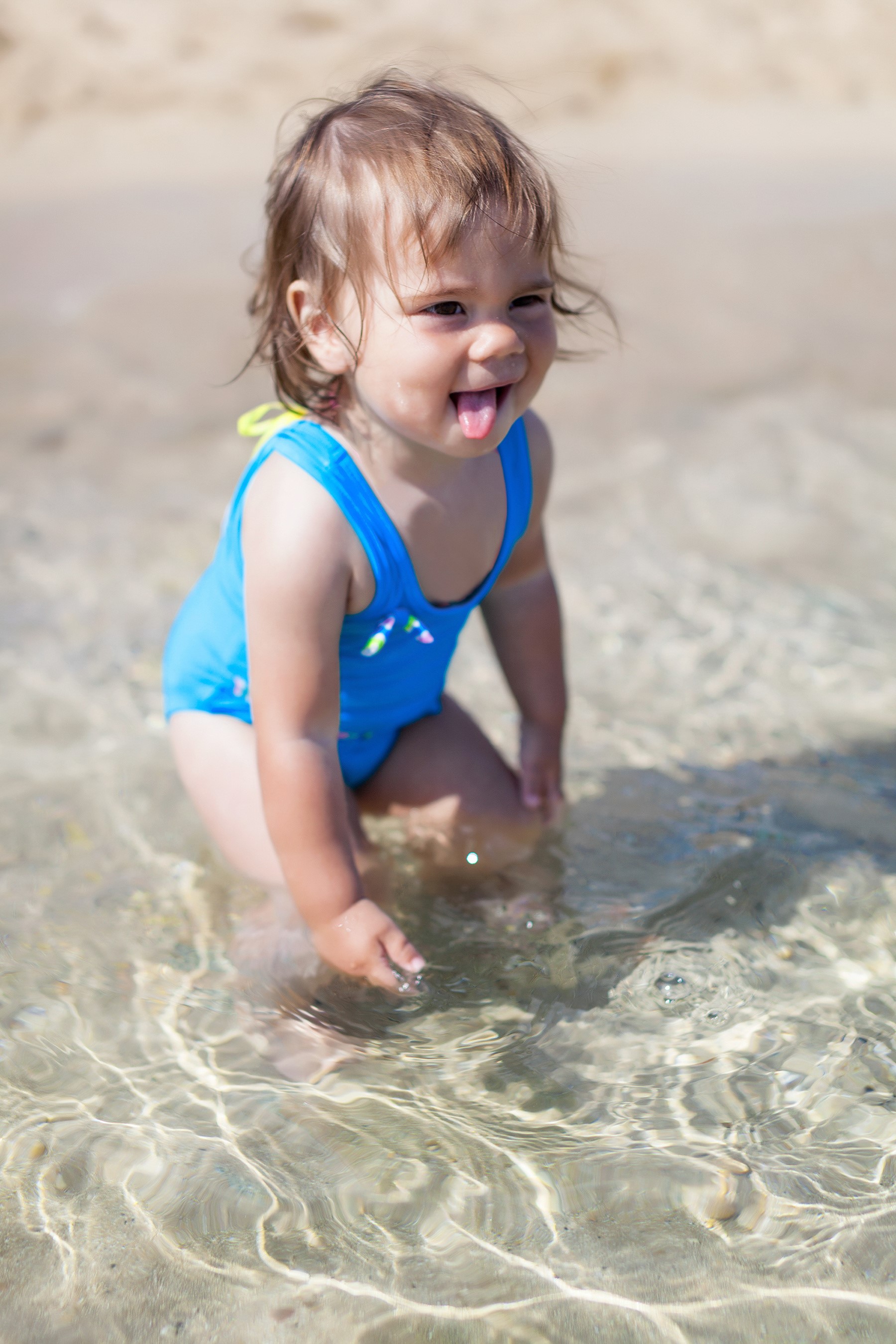 Baby girl in blue swimsuit playing in shallow water HD Phone Wallpaper