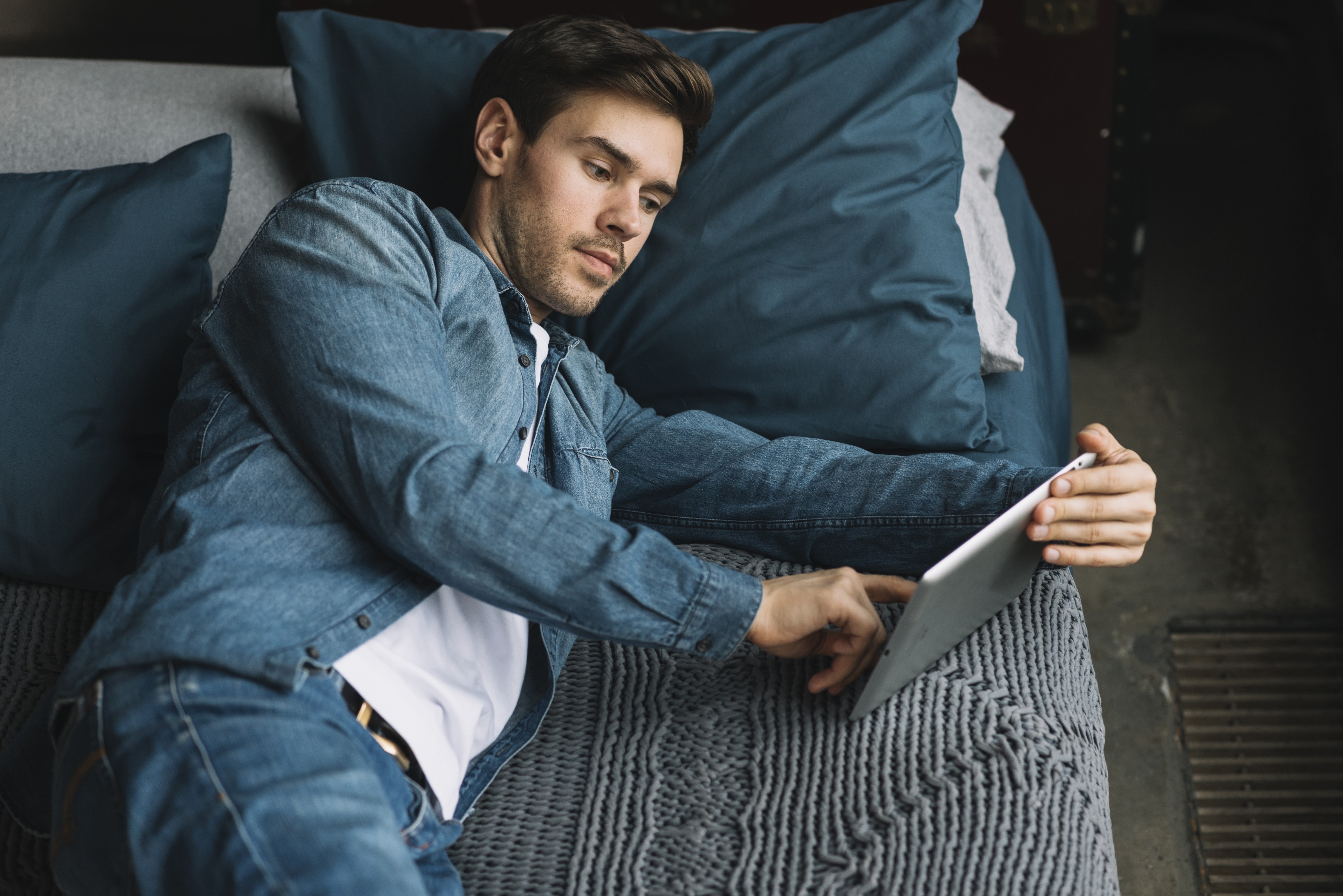 Man in denim shirt using a tablet on a bed HD Wallpaper