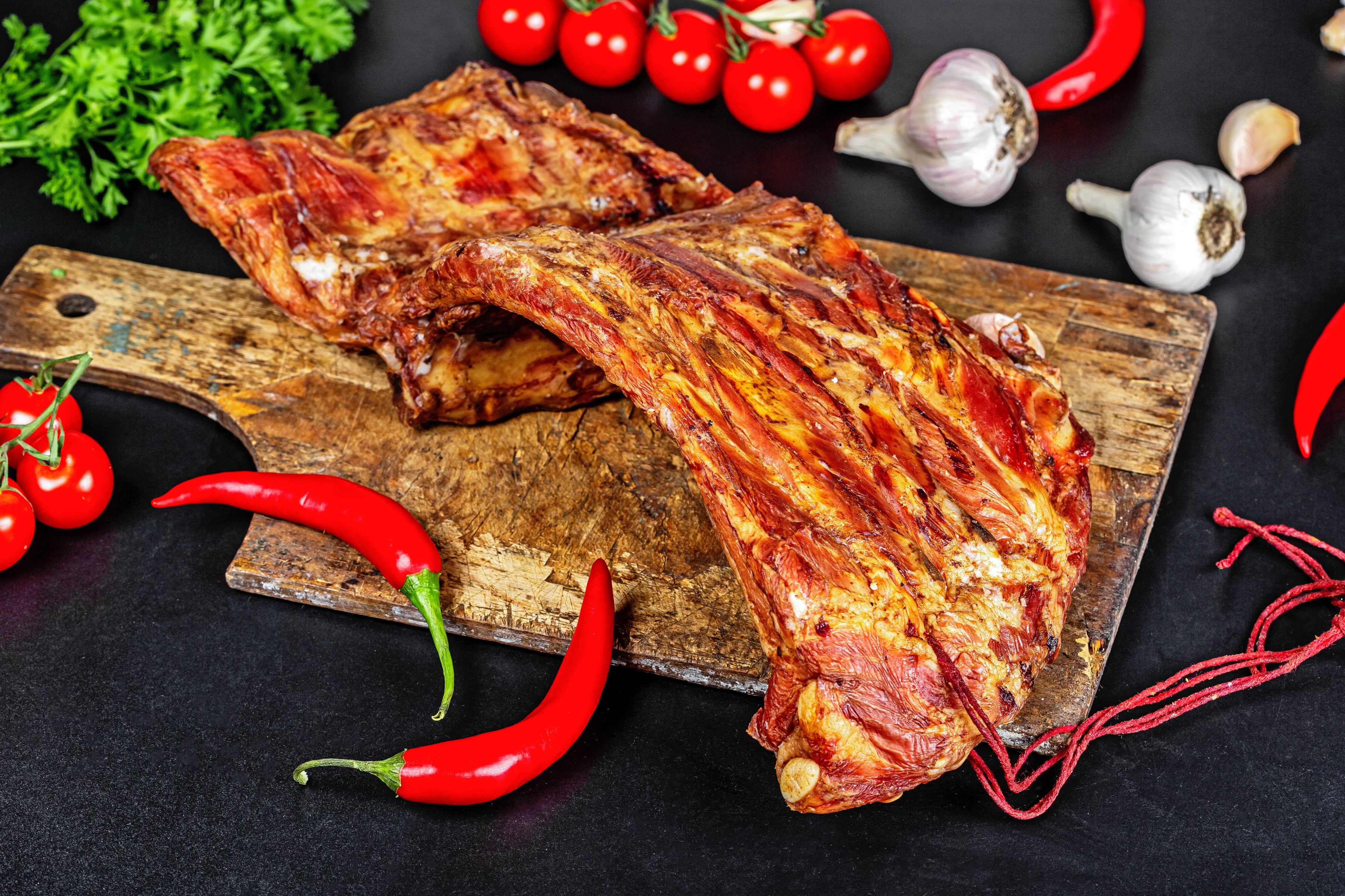 Smoked ribs with chili peppers, garlic, and tomatoes on a cutting board HD Wallpaper