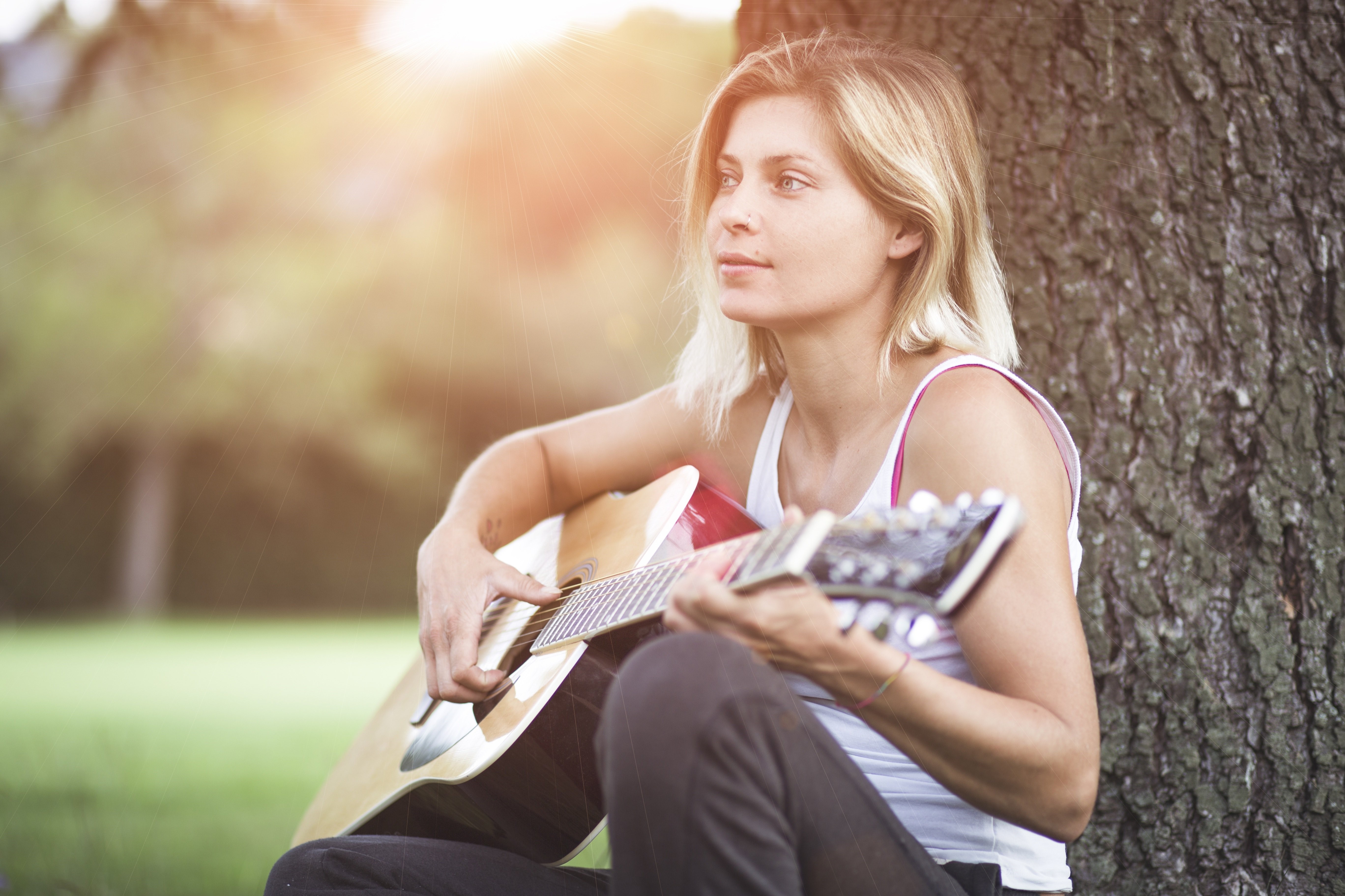 Blonde girl playing guitar sitting by a tree HD Wallpaper