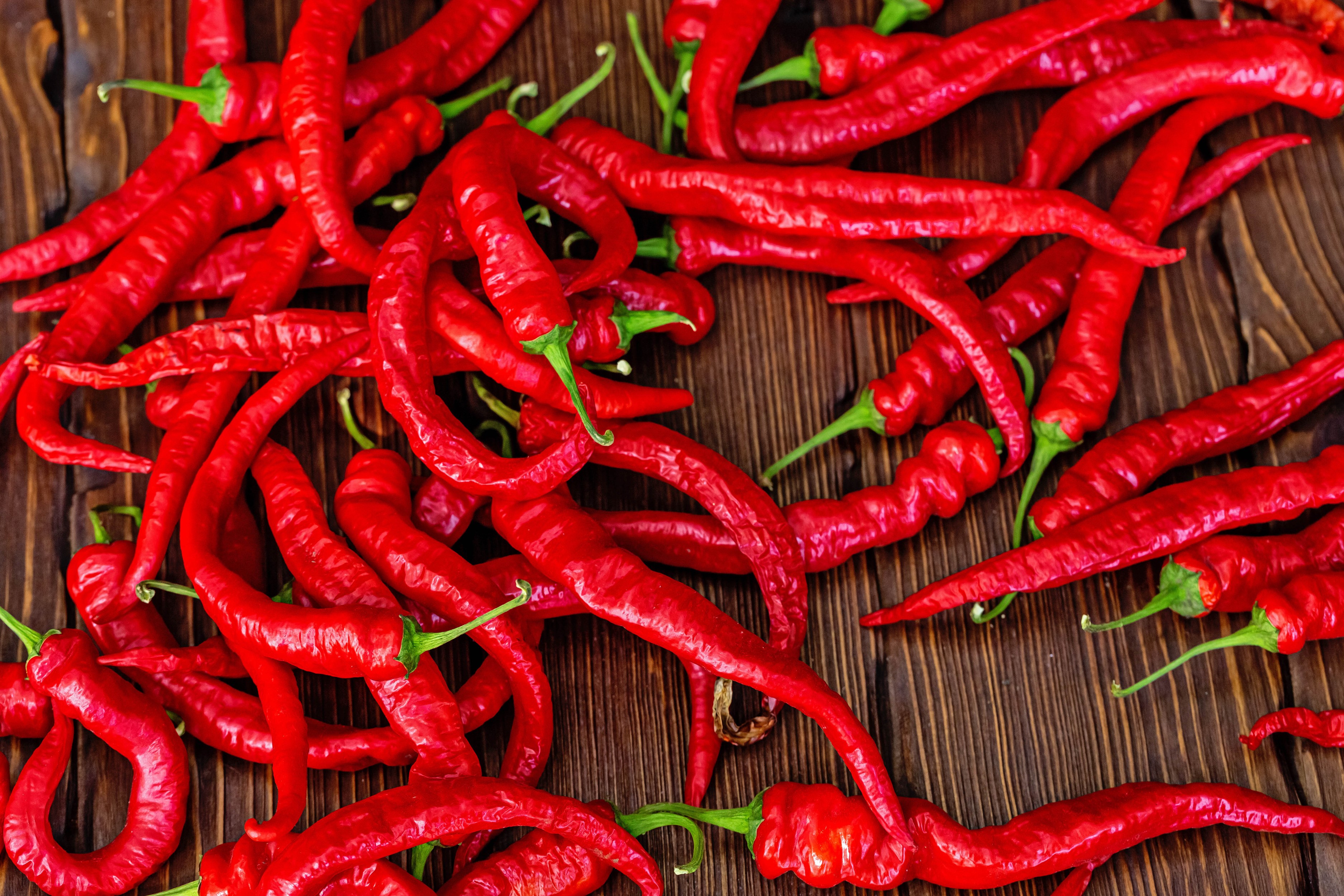 Pile of red chili peppers on a wooden surface HD Wallpaper